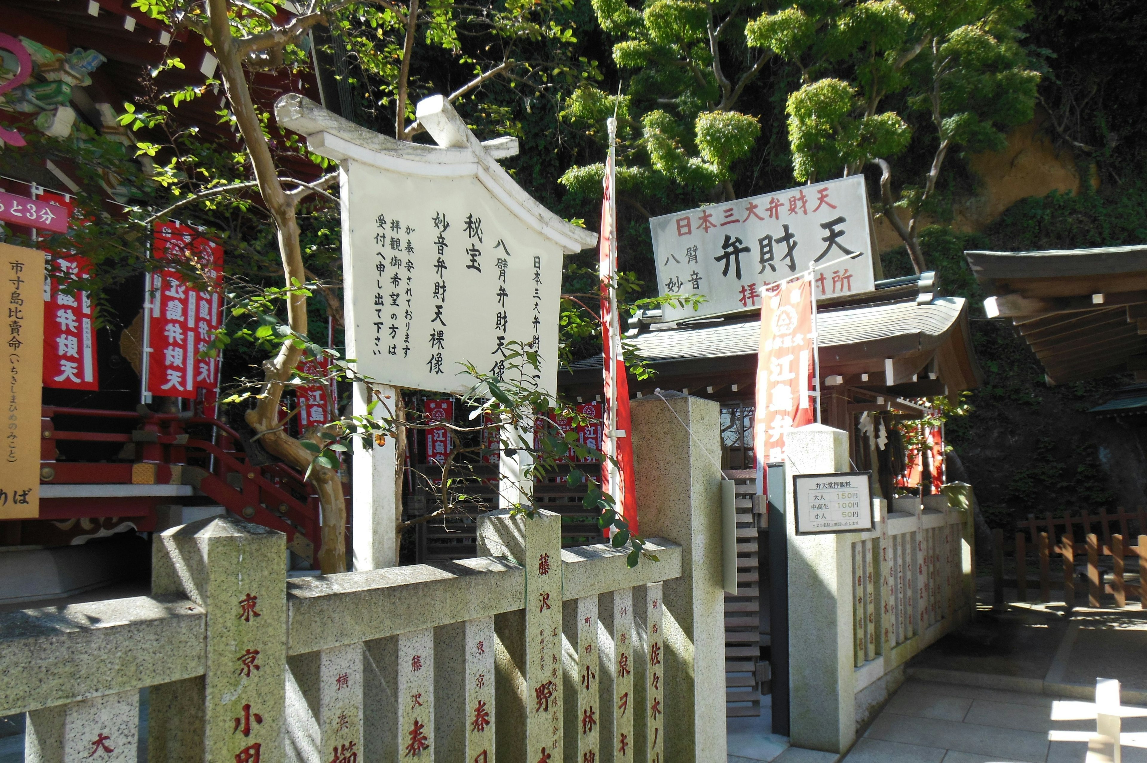 神社の入り口にある白い看板と赤い提灯が見える