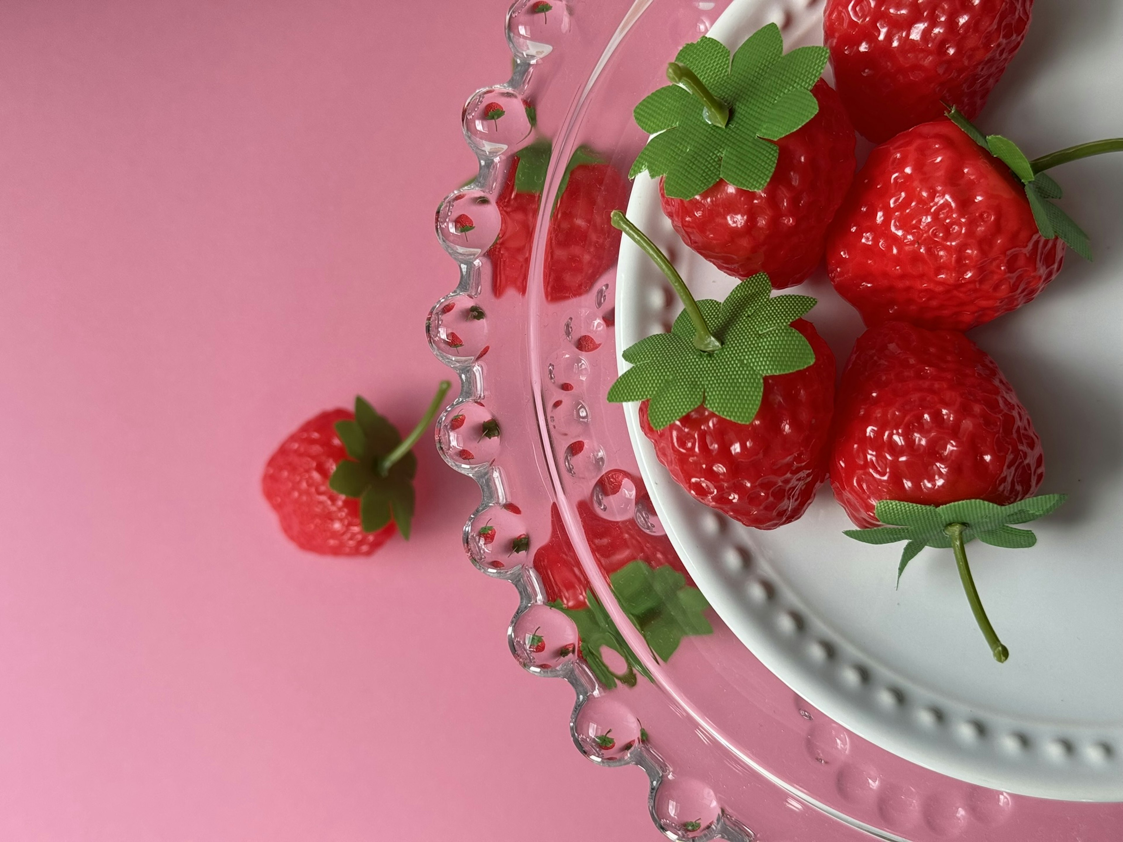 Vibrant red strawberries arranged on a white plate with a pink background and crystal serving stand