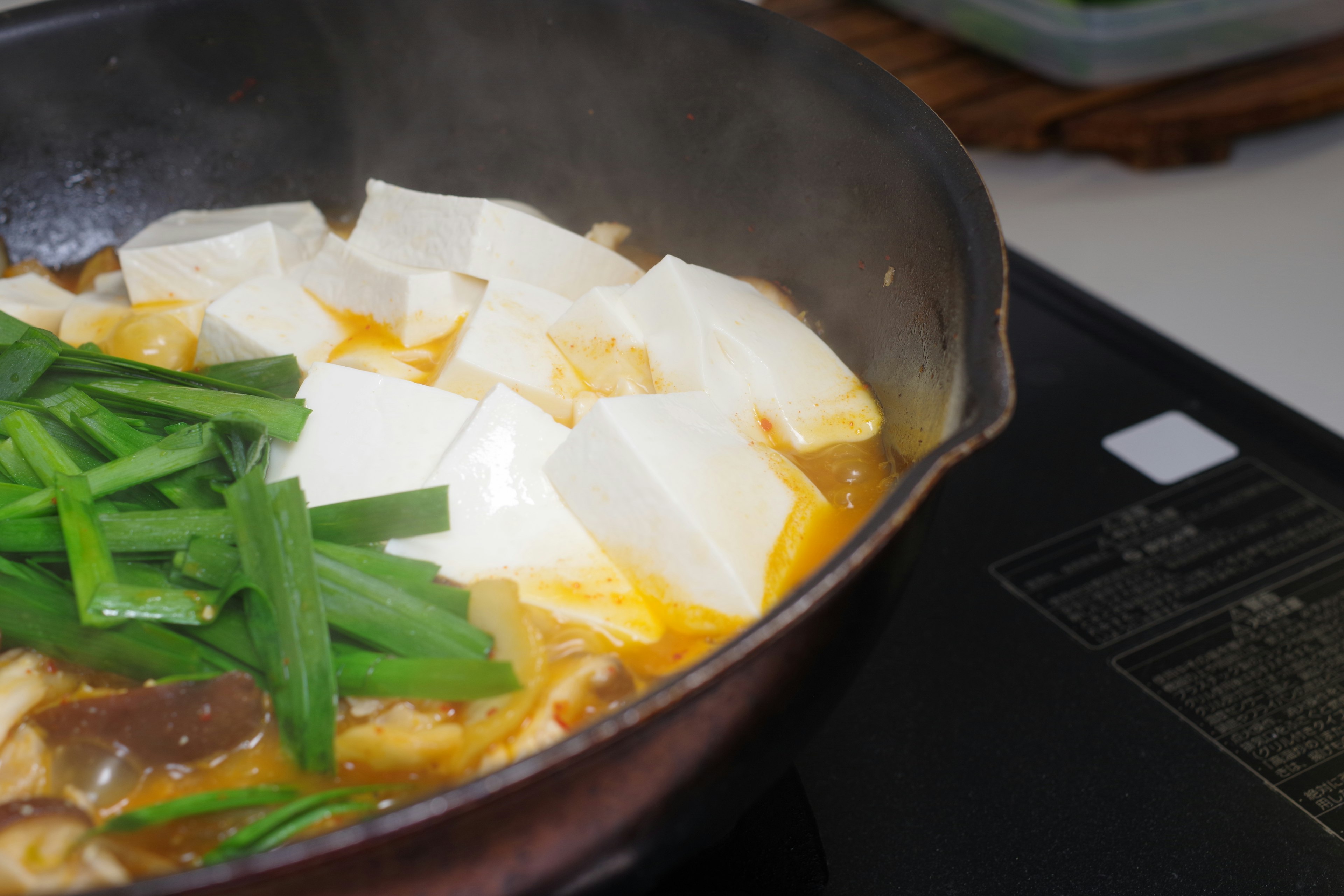 Une casserole contenant du tofu et des oignons verts dans un bouillon