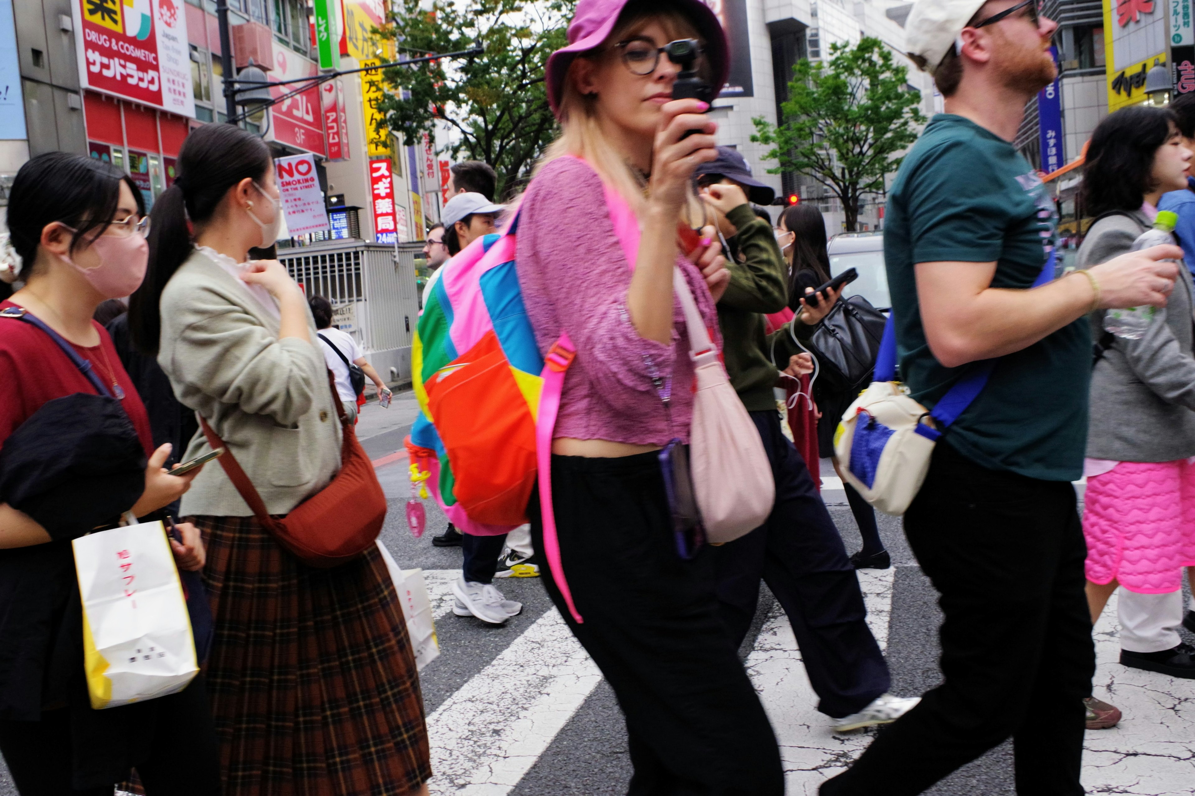 Multitud de personas cruzando una calle concurrida mujer con bolsa colorida y cámara ropa vibrante