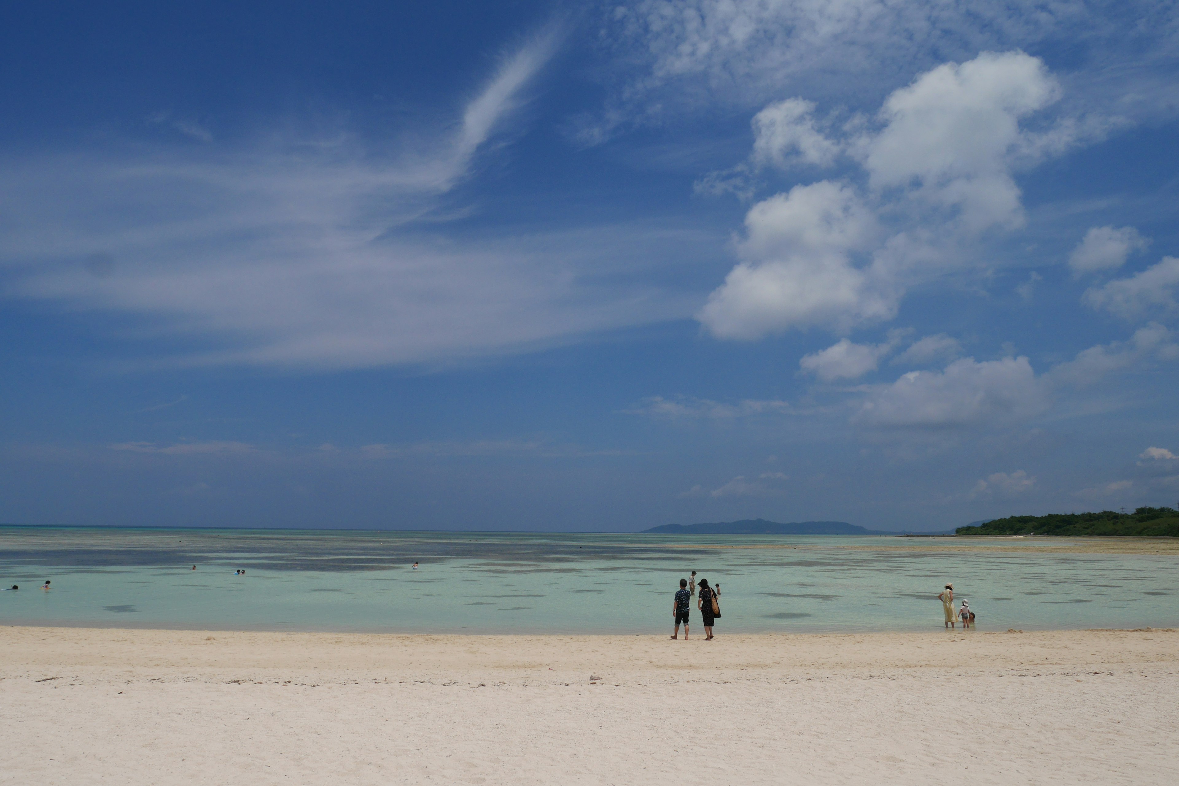 เงาคนสองคนยืนอยู่บนชายหาดที่สวยงามท่ามกลางท้องฟ้าและทะเลสีฟ้า