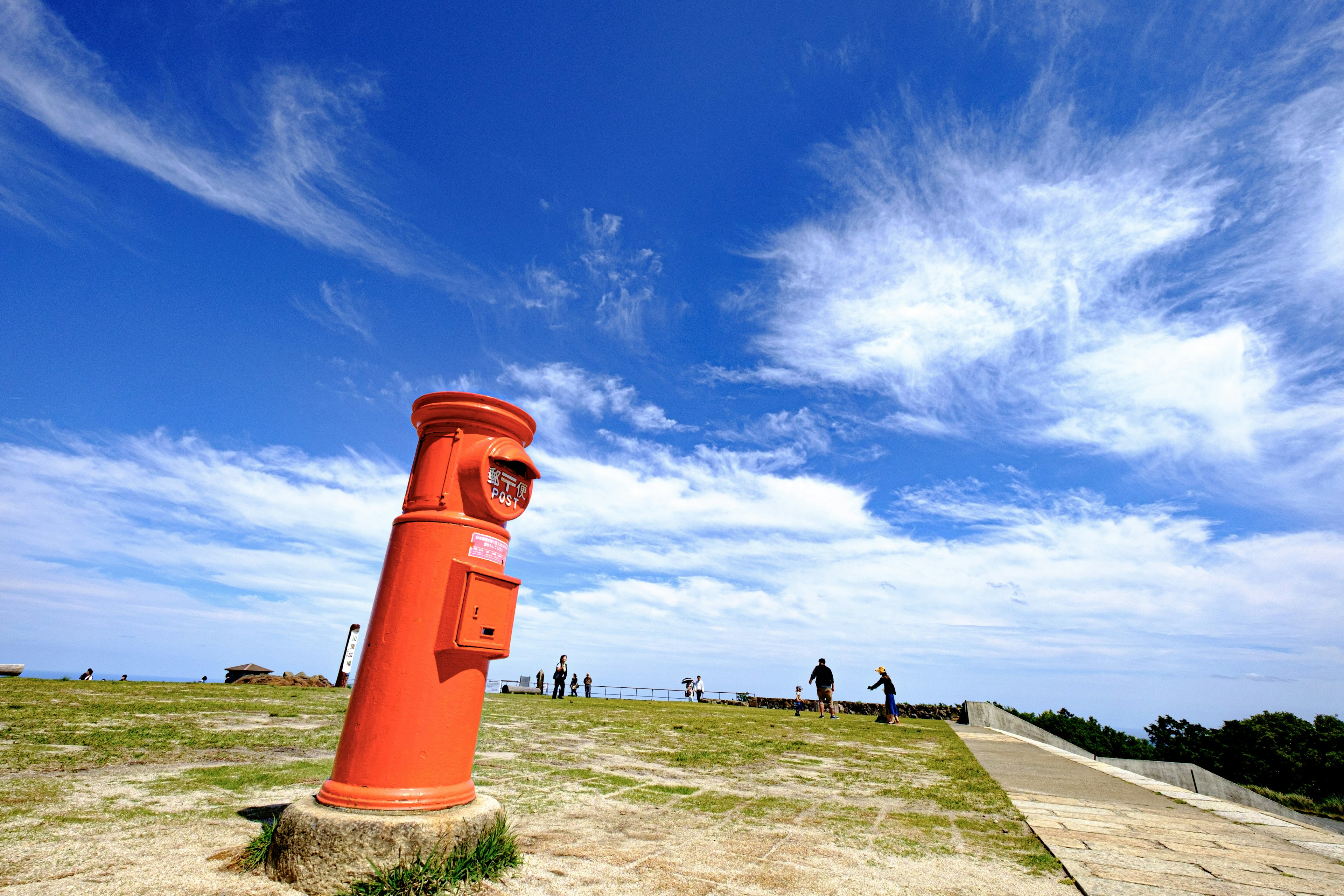 Red mailbox standing under a blue sky with distant figures