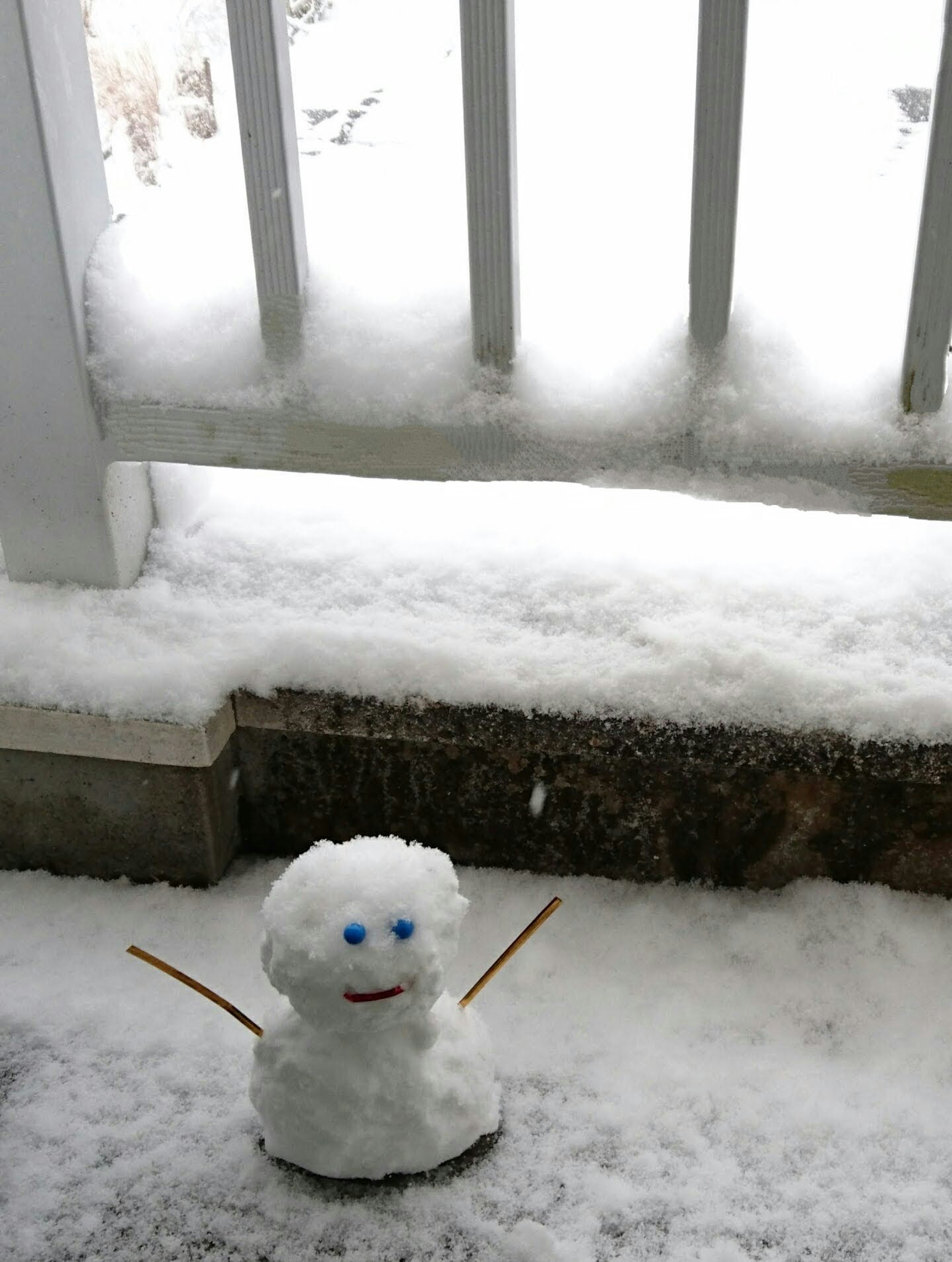 A snowman standing in the snow with blue eyes and stick arms