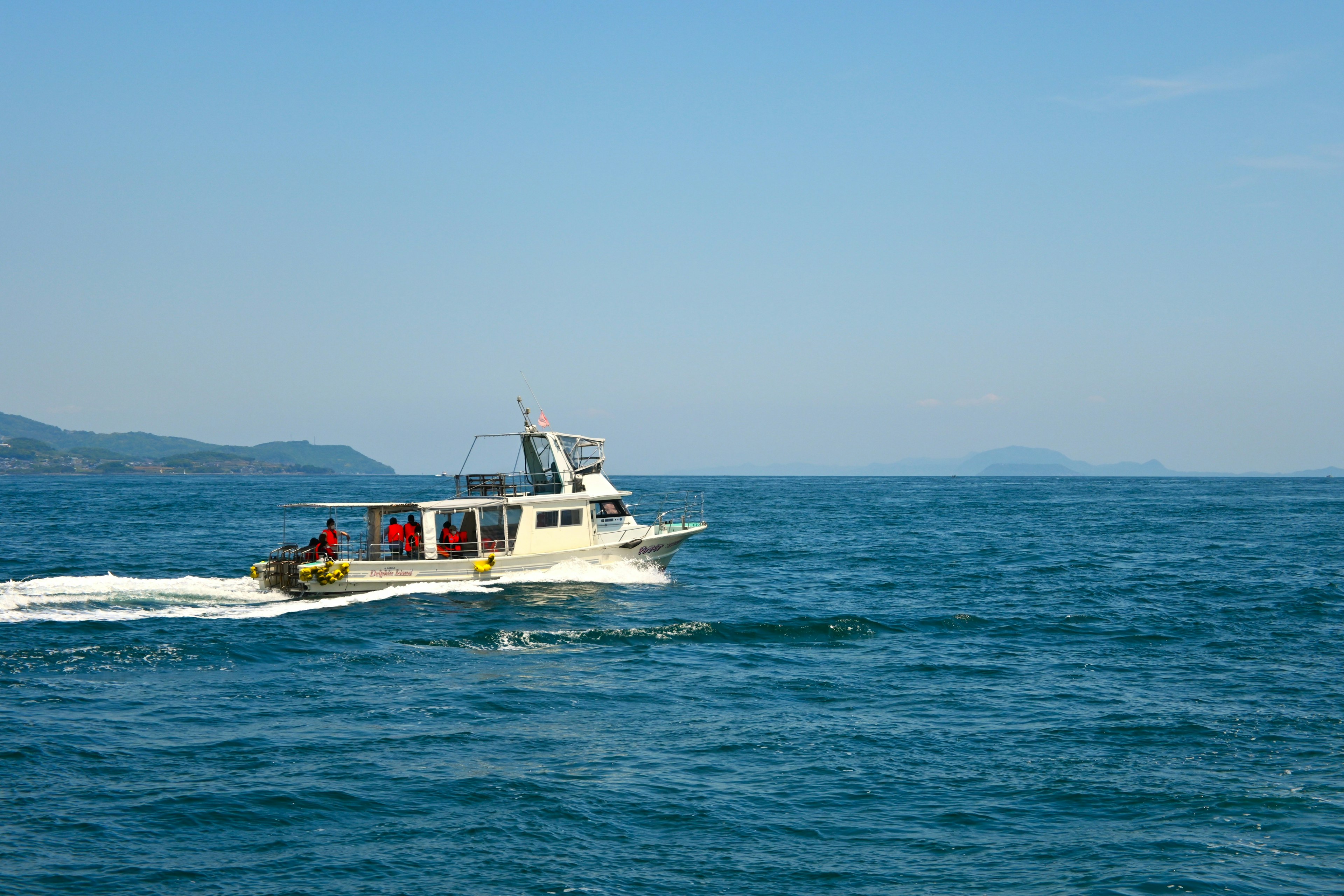 青い海を航行する小型ボートとその周囲の山々