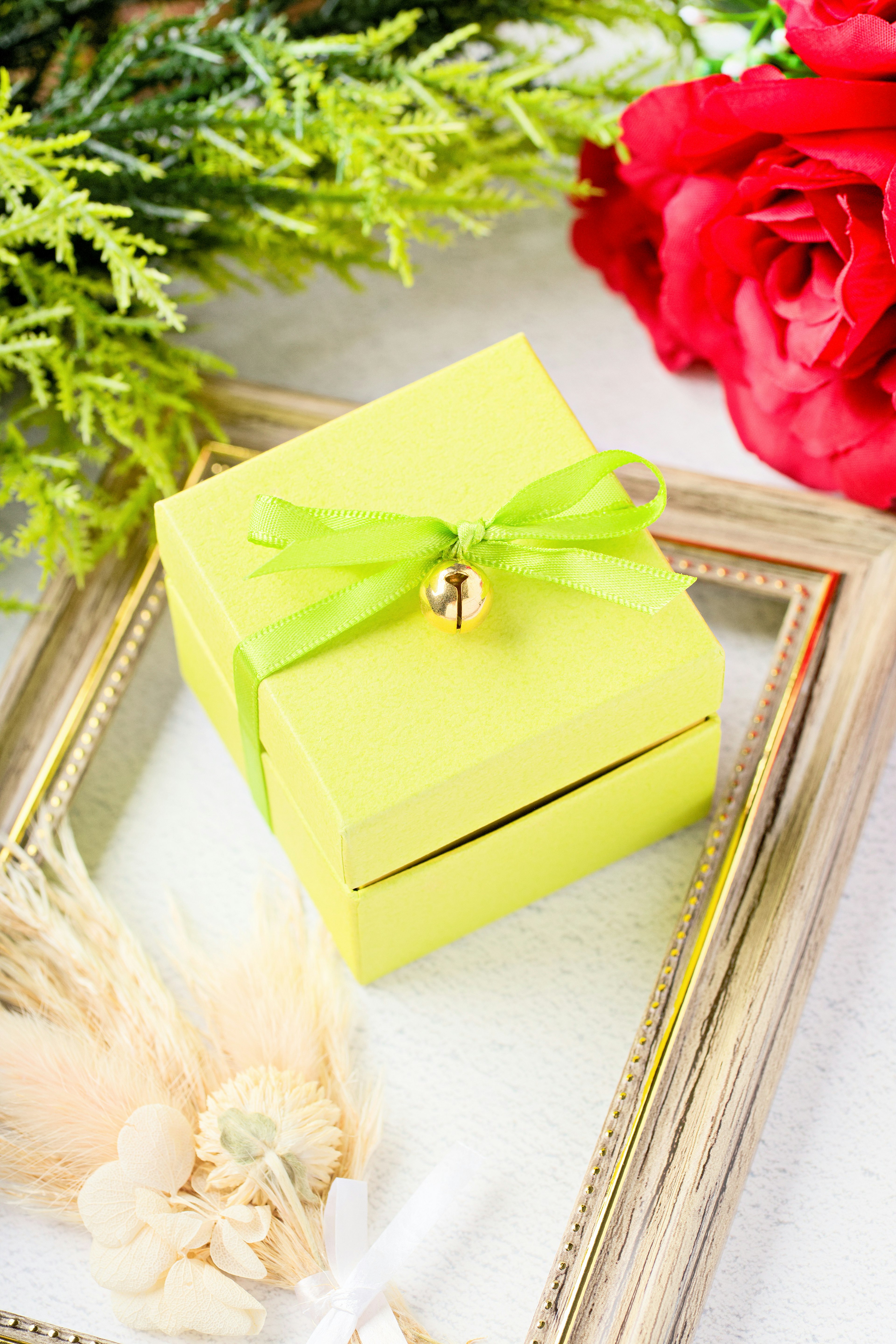 Boîte-cadeau jaune avec un ruban vert et une cloche entourée de roses rouges et de verdure