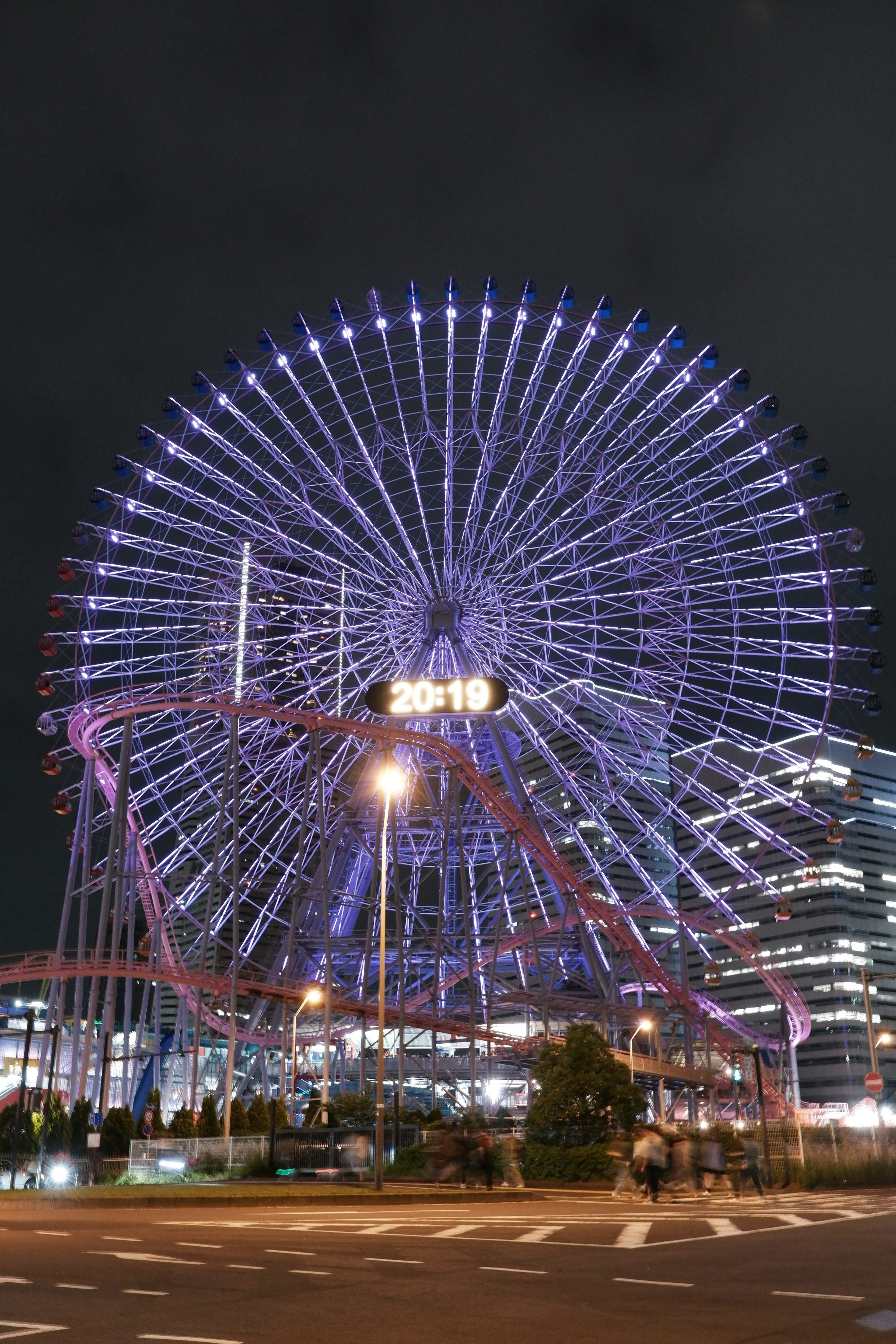 Night view of a Ferris wheel with illuminated lights and surrounding buildings