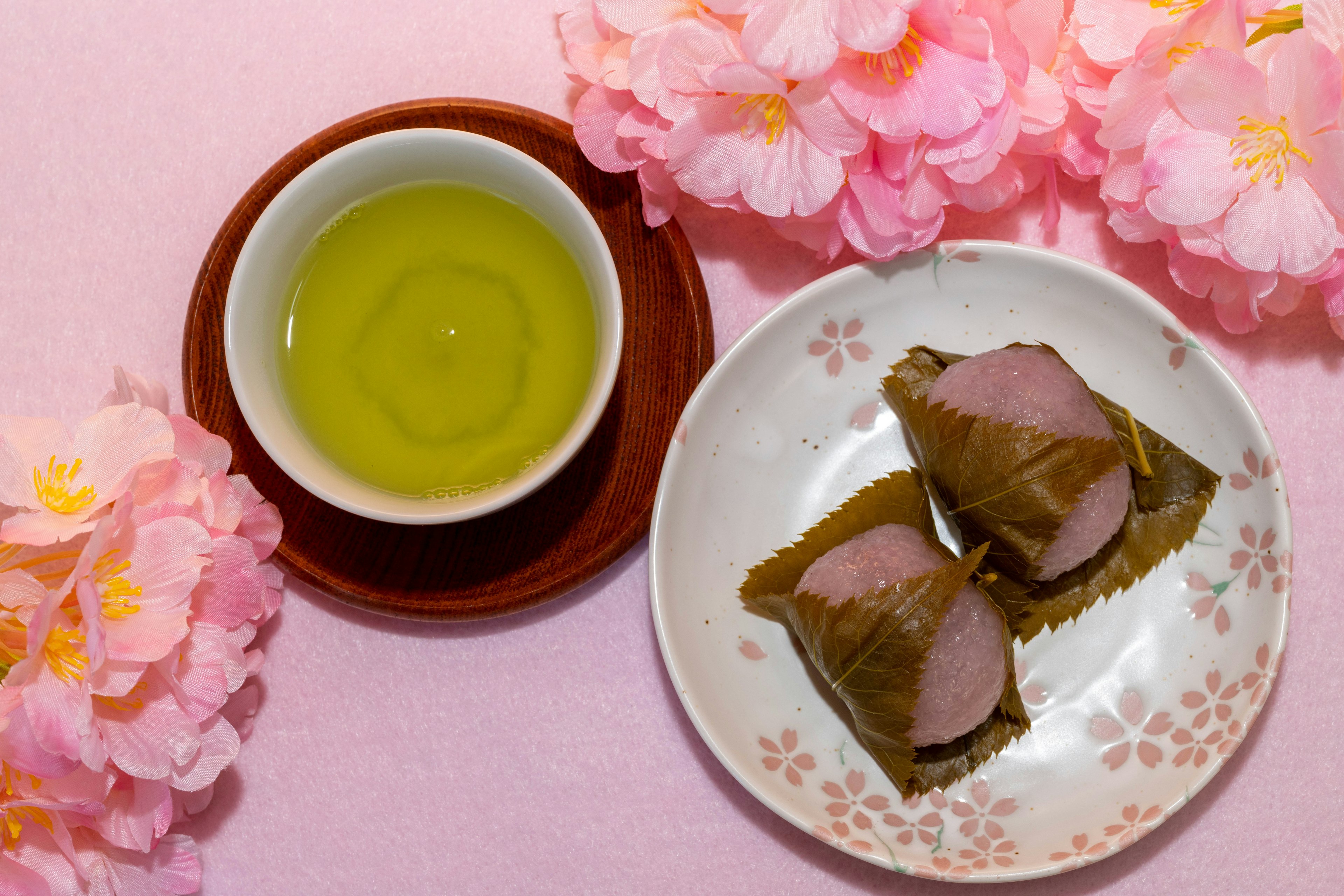 Una scena con tè verde e dolci tradizionali circondati da fiori di ciliegio