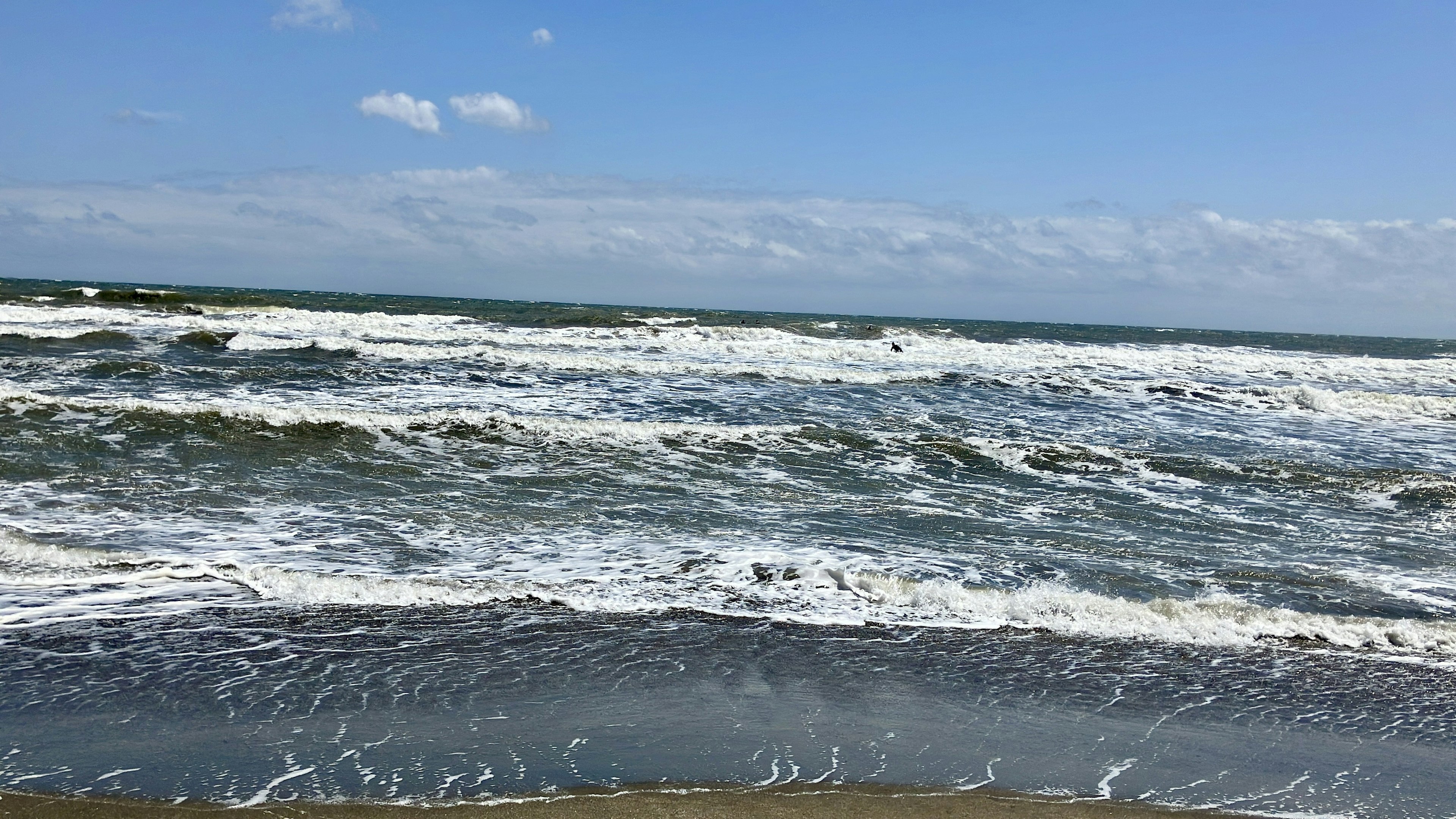 Wellen brechen am Ufer unter einem blauen Himmel