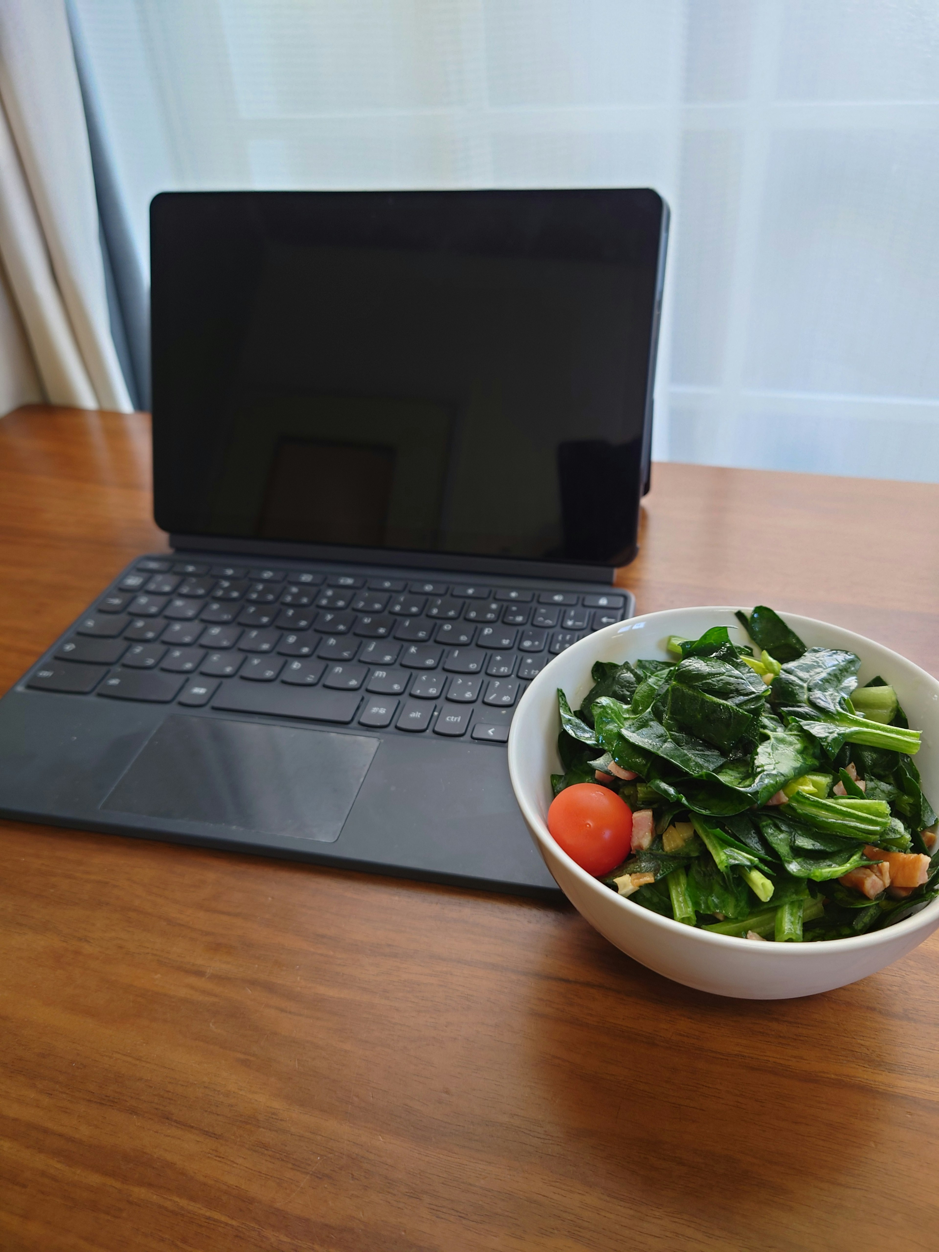 Una computadora portátil y un tazón de ensalada sobre una mesa de madera