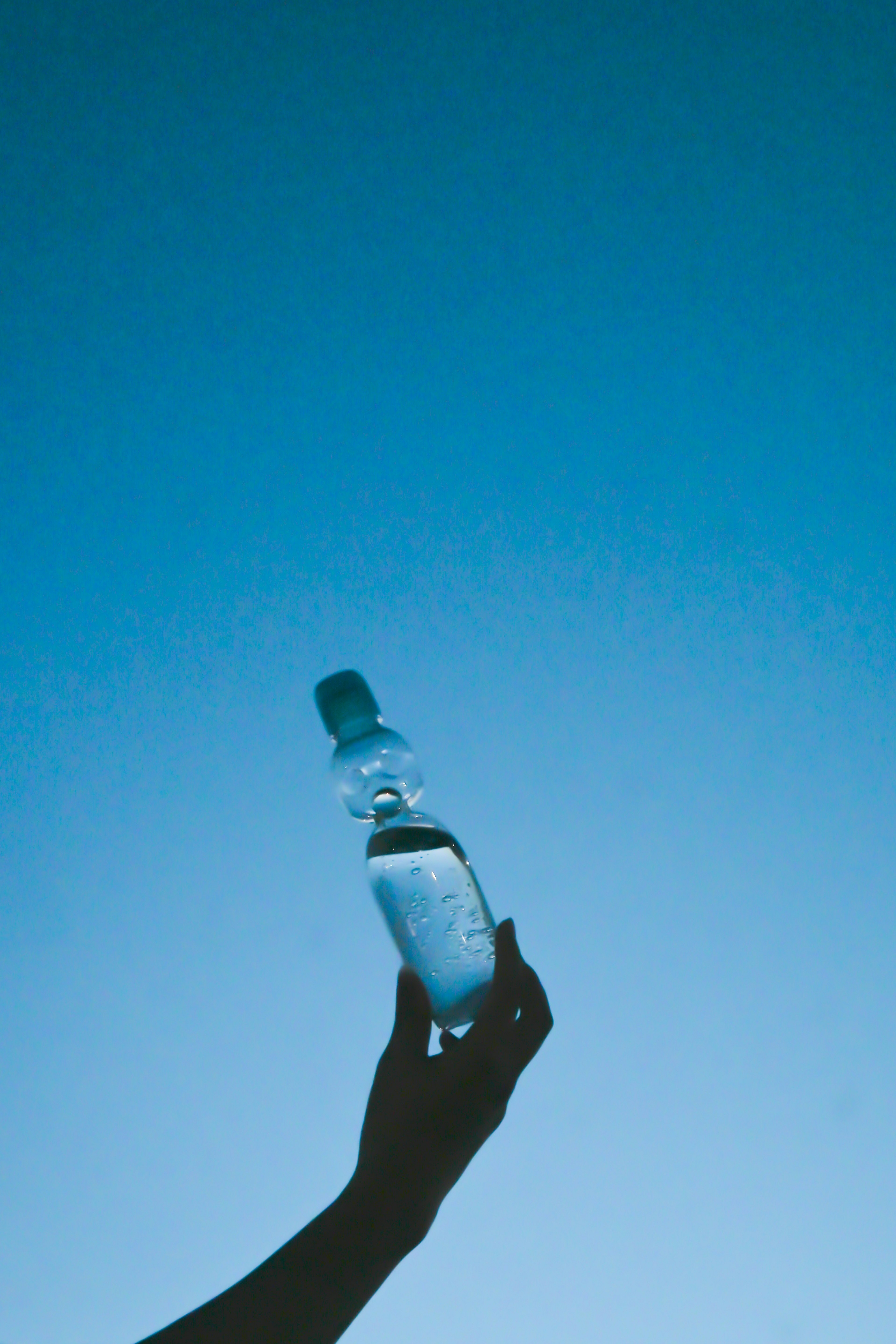 Silhouette di una mano che tiene una bottiglia d'acqua contro un cielo blu