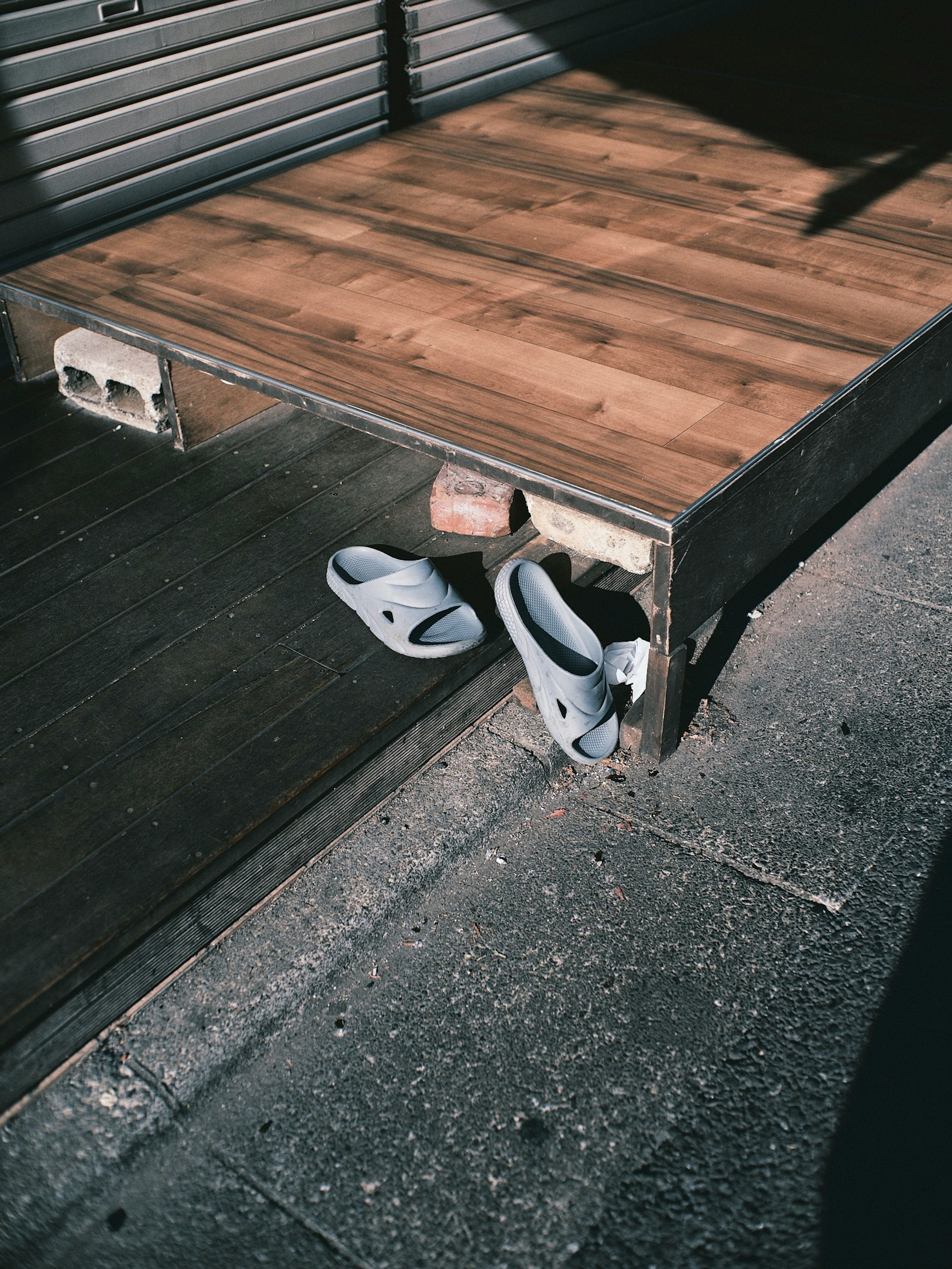 Sandals partially hidden under a wooden platform with shadows