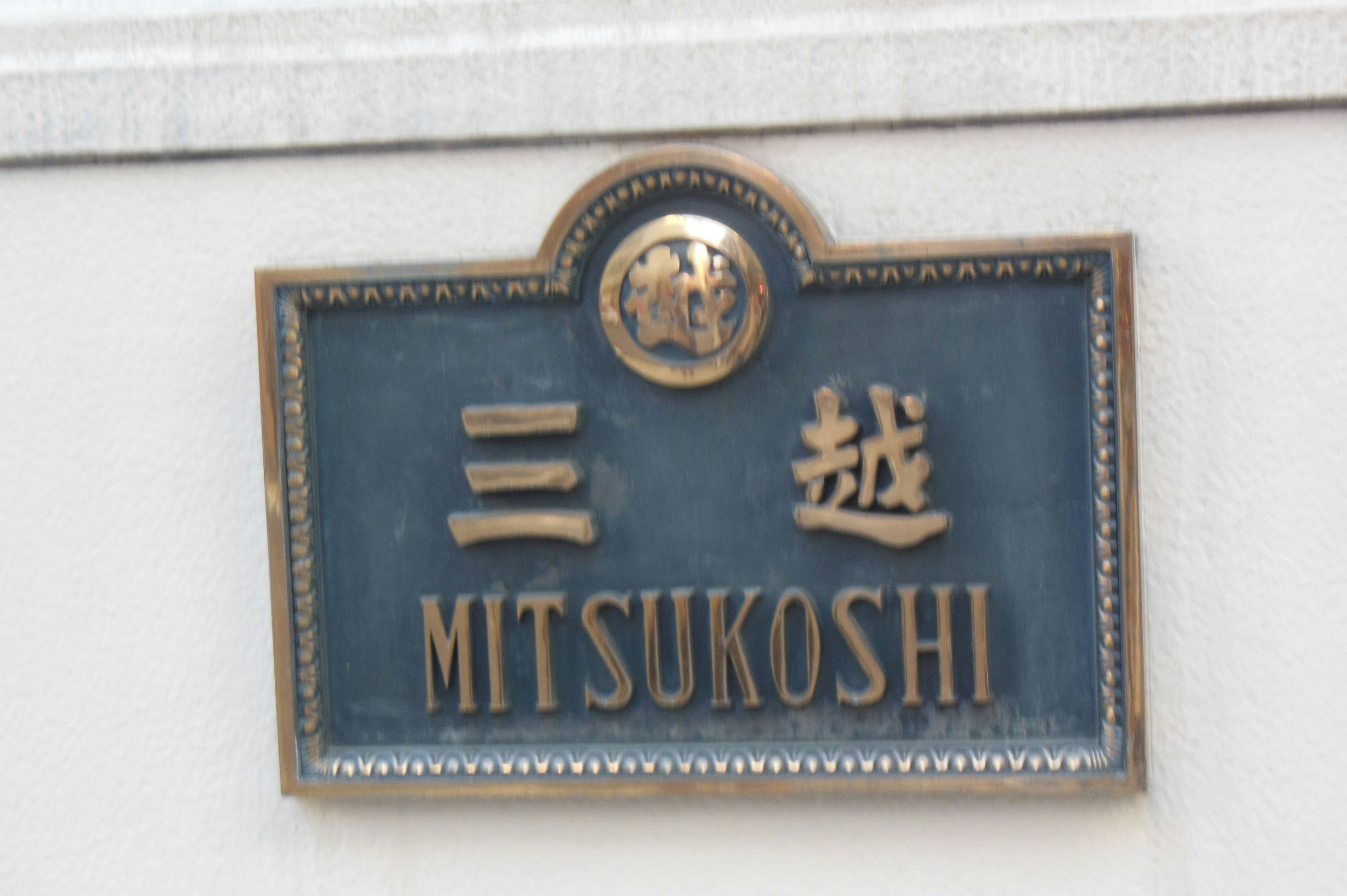 Panneau Mitsukoshi affiché sur un fond bleu avec des lettres dorées