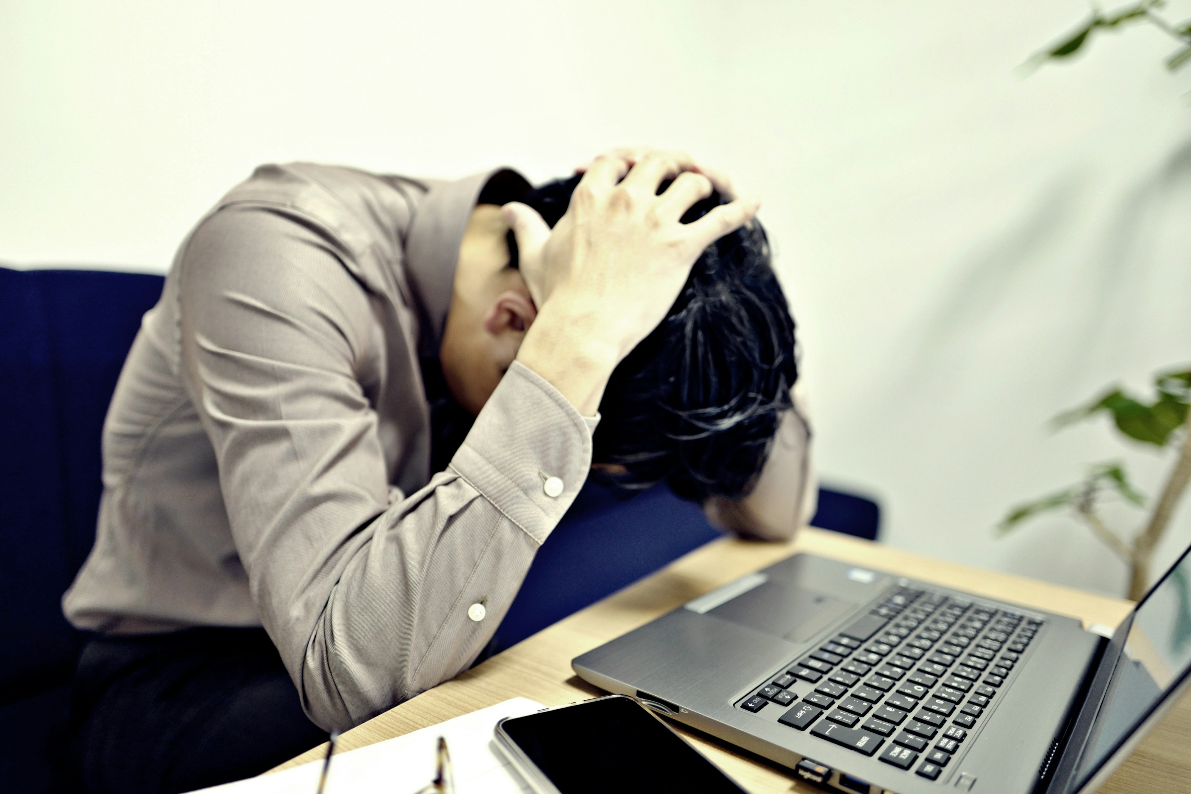 A man in a button-up shirt holding his head in frustration at a laptop