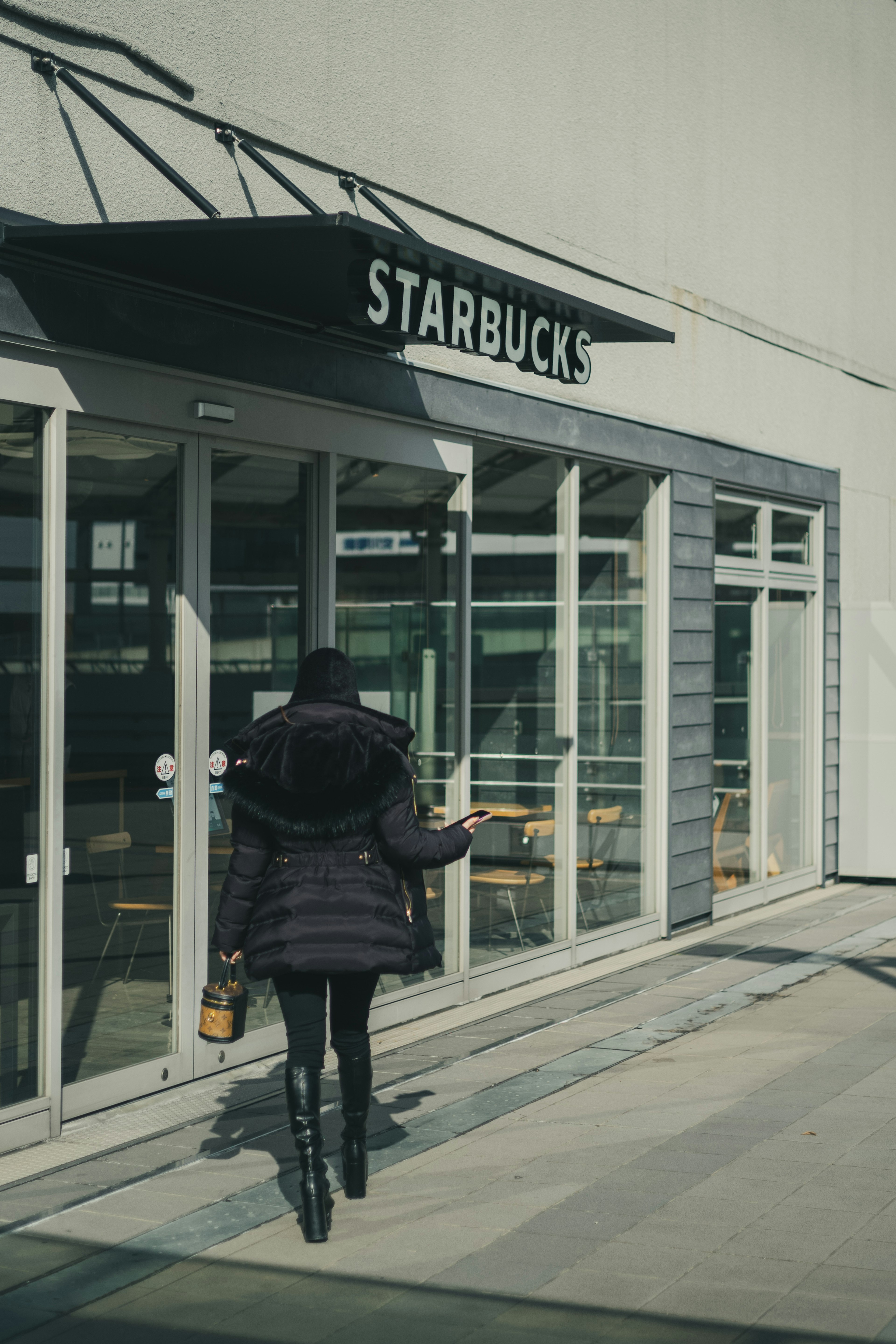 Donna che cammina verso l'ingresso di Starbucks indossando un cappotto nero