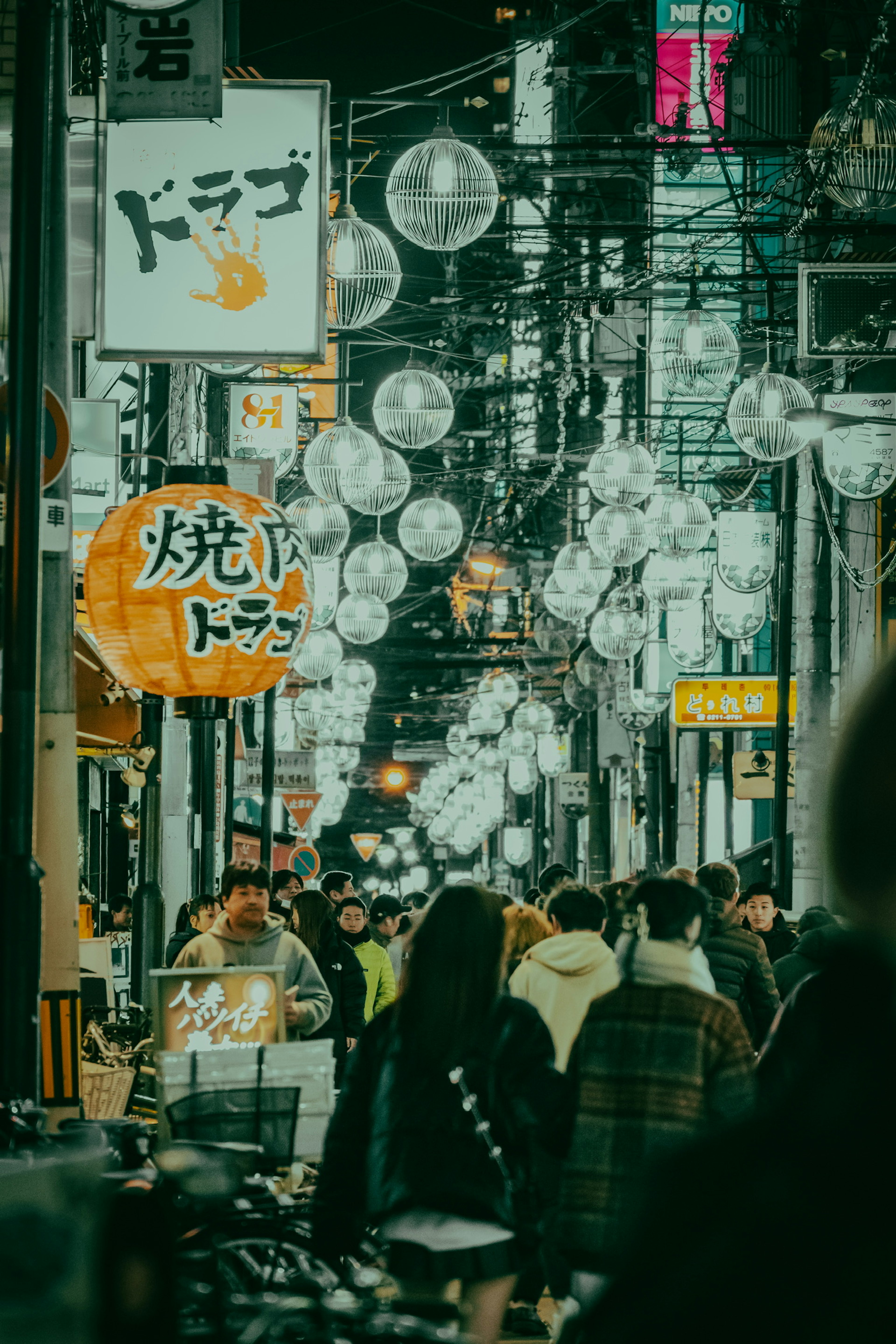 Crowded street at night with hanging lights and various signs