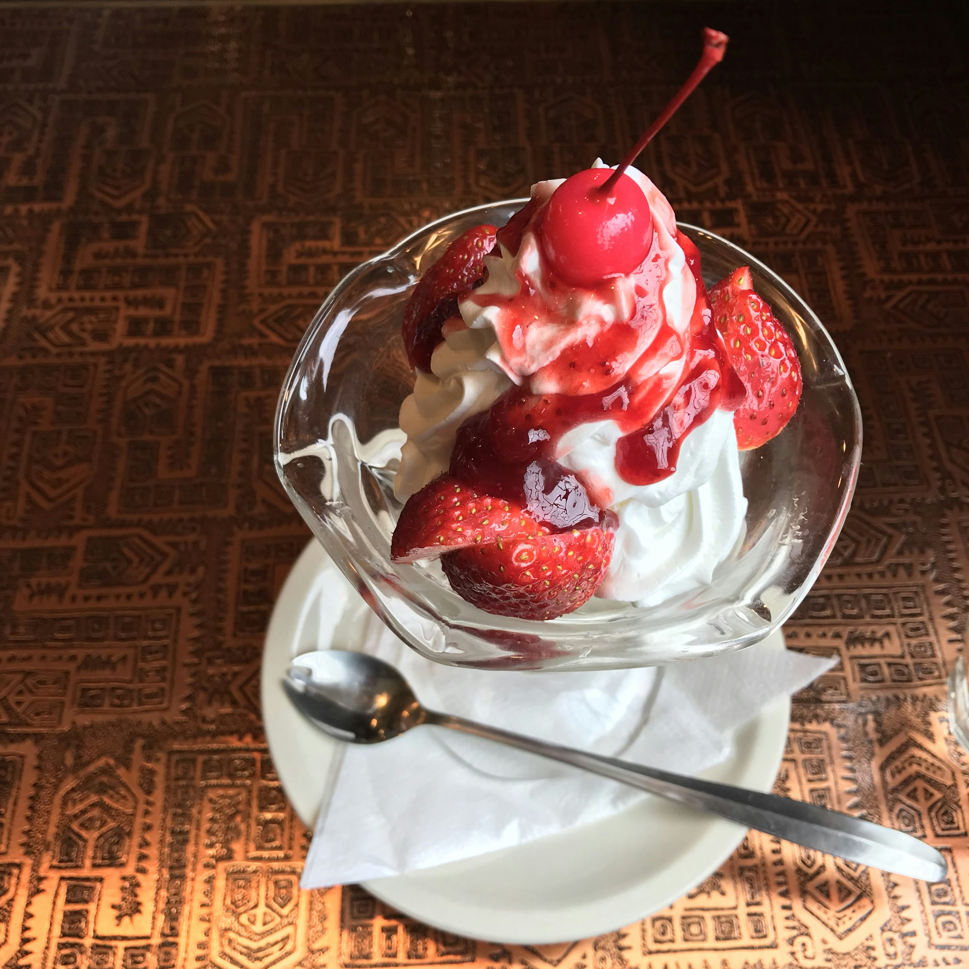 Coppa di gelato con fragole e una ciliegia servita in un piatto di vetro