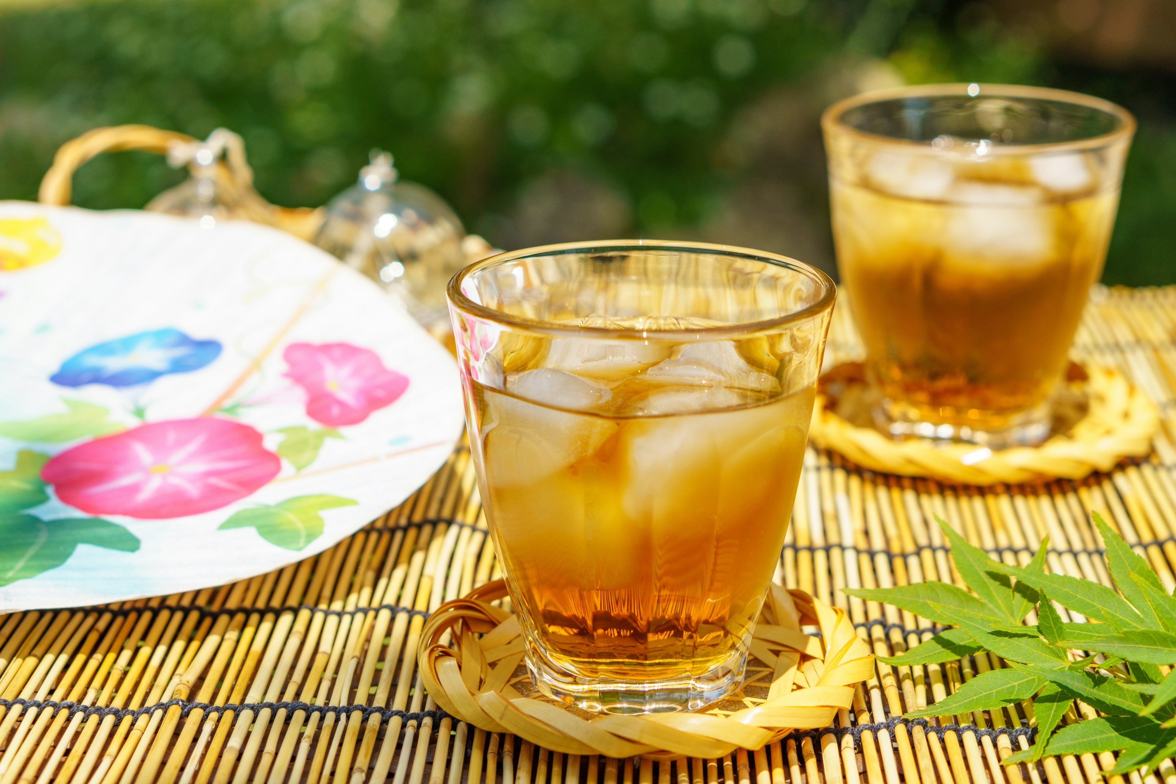 Dos vasos de té helado sobre un tapete de bambú con un plato floral colorido