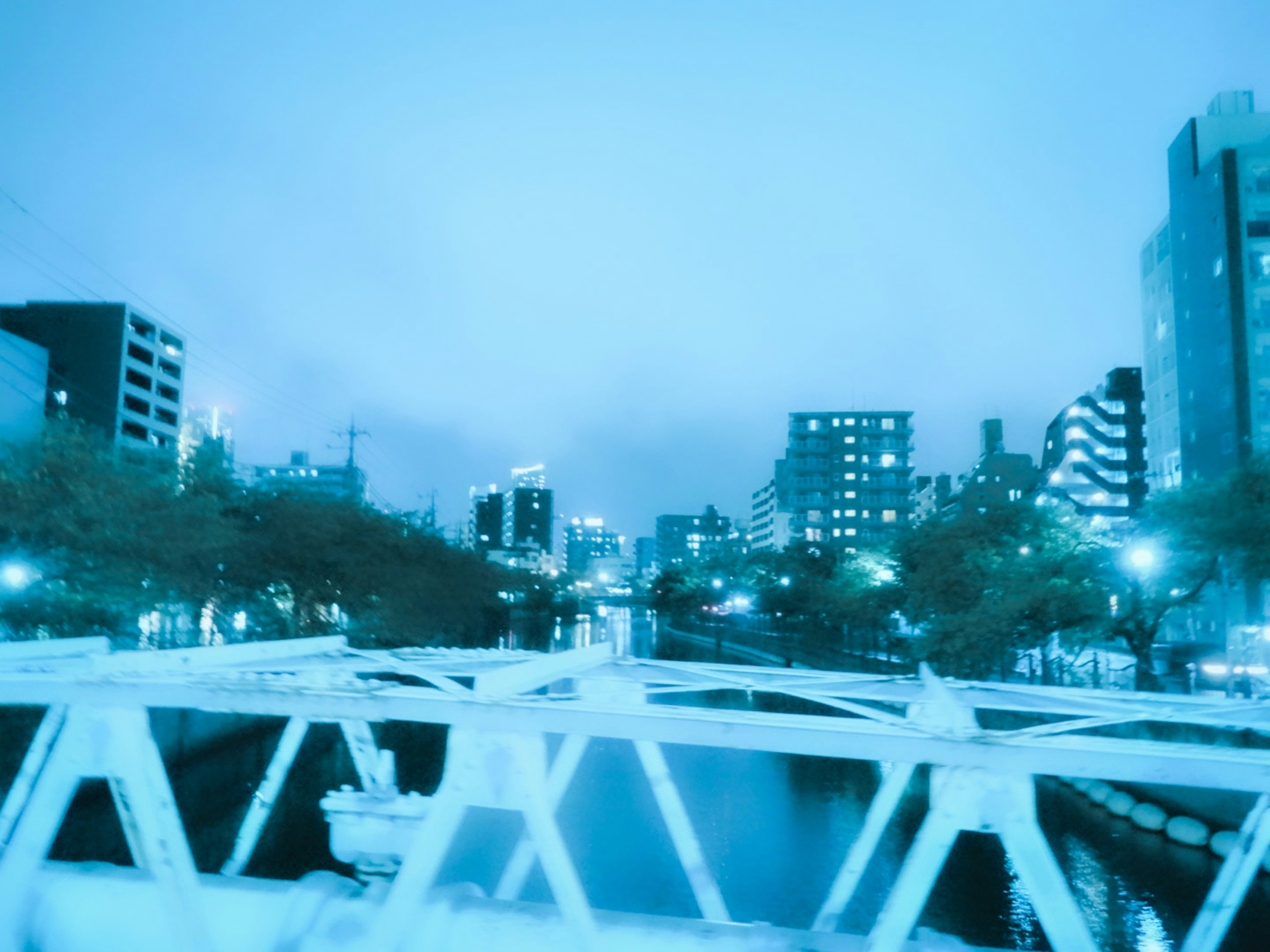 Blautonige Nachtstadtansicht mit einer Brücke über einen Fluss