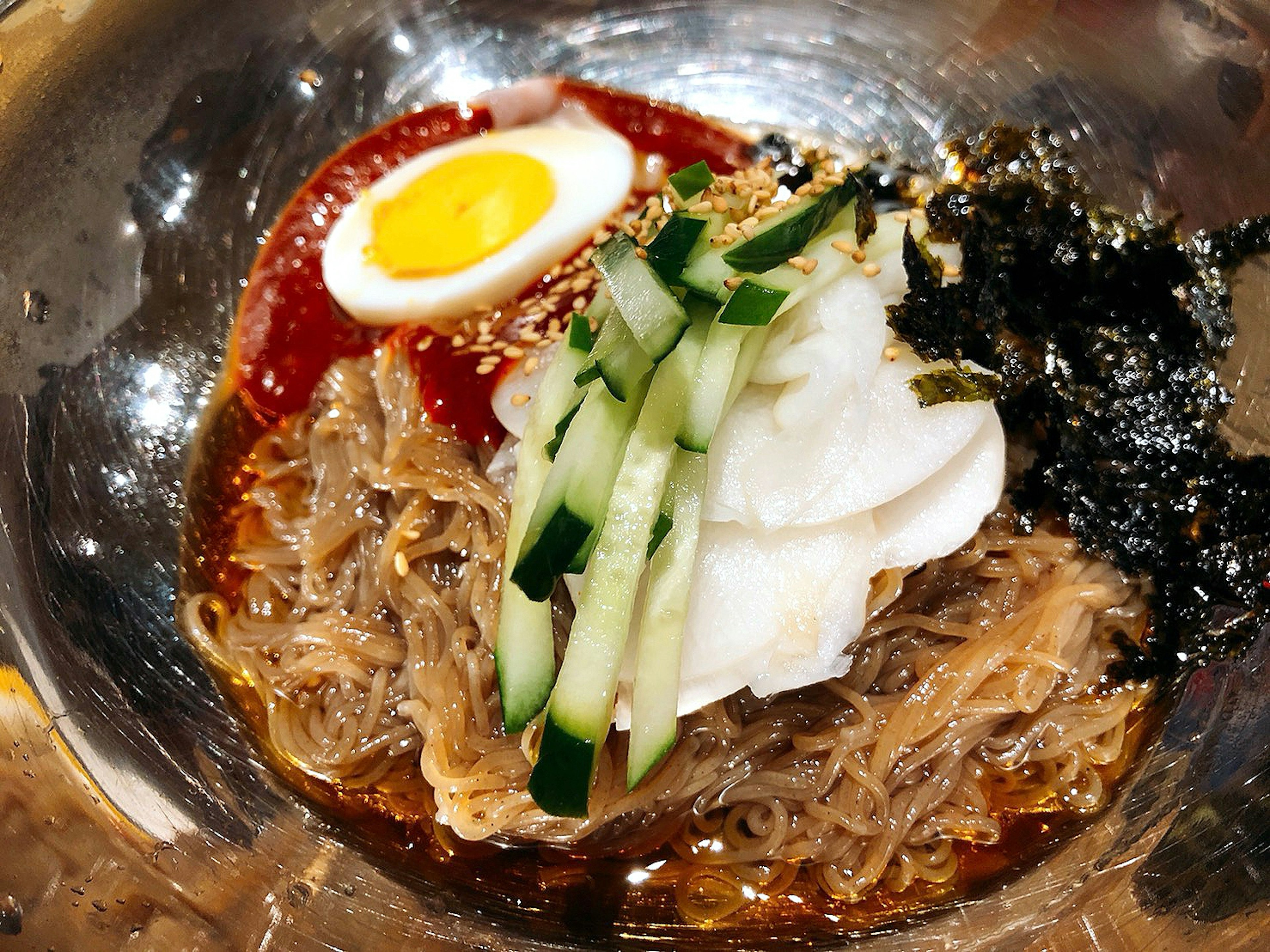 Una ciotola di noodle freddi guarnita con un uovo alla coque cetriolo alga semi di sesamo e salsa piccante