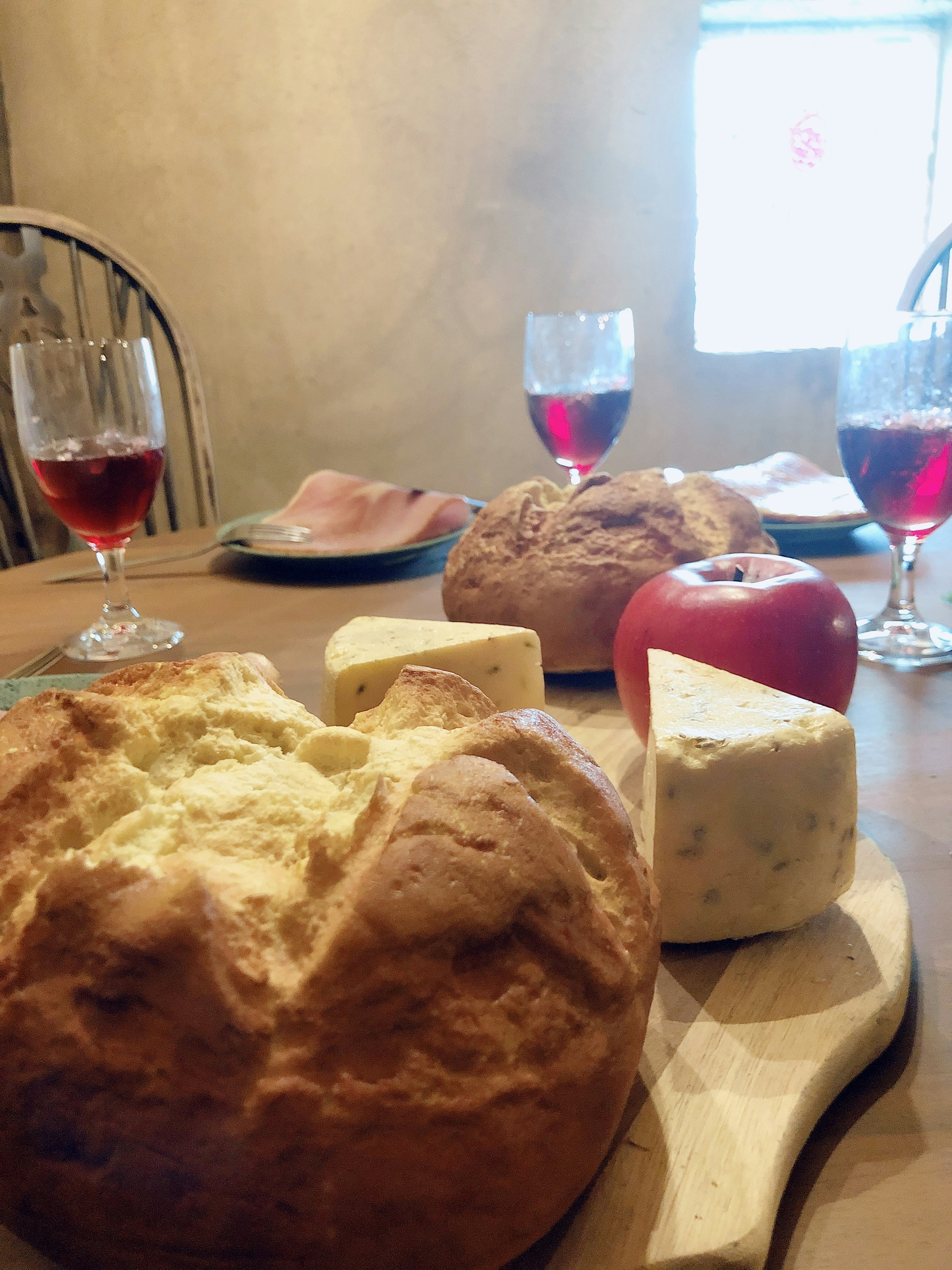 Bread, cheese, apple, and red wine glasses on a wooden table