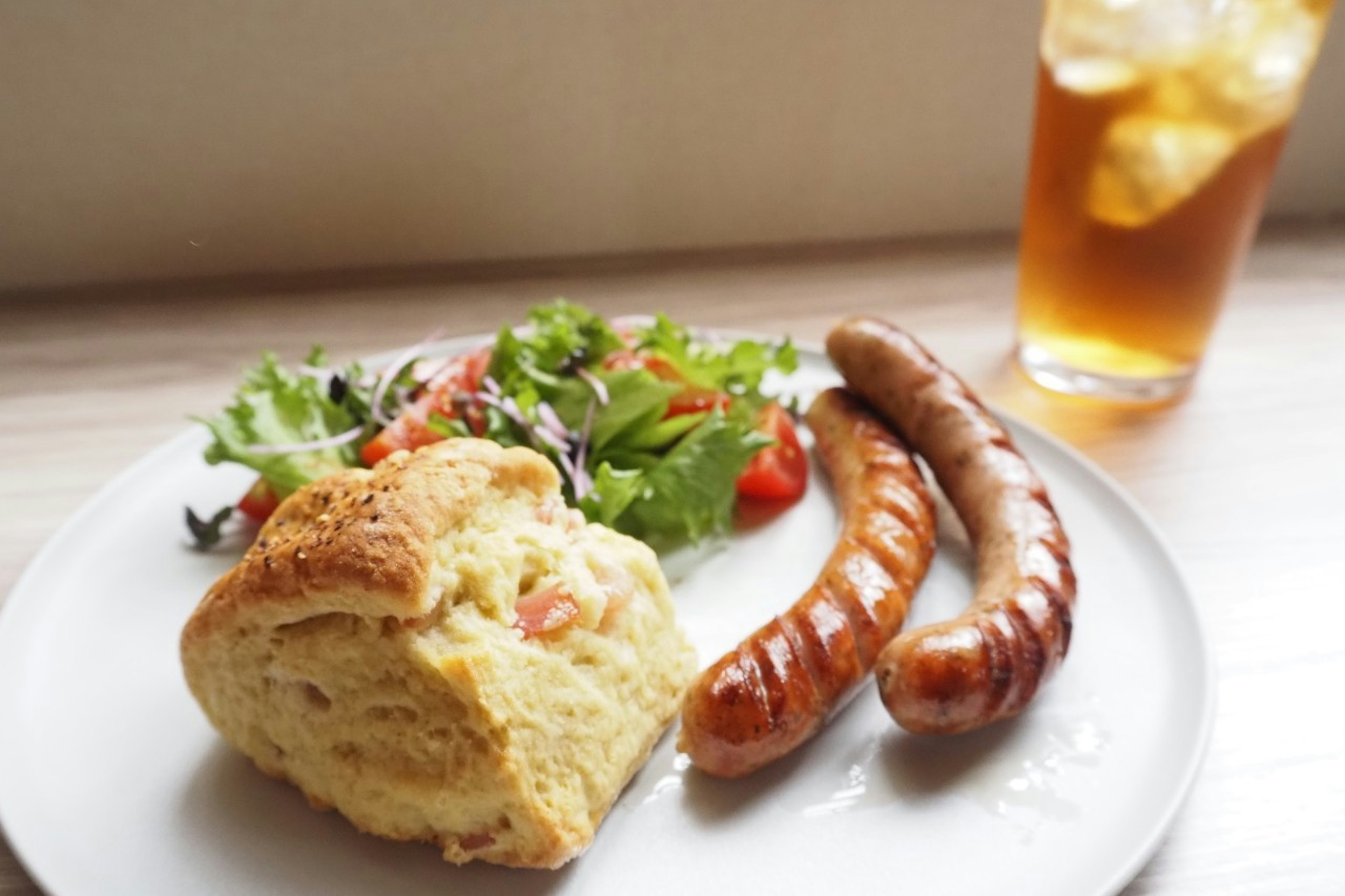 Plate with salad, sausages, biscuit, and iced tea