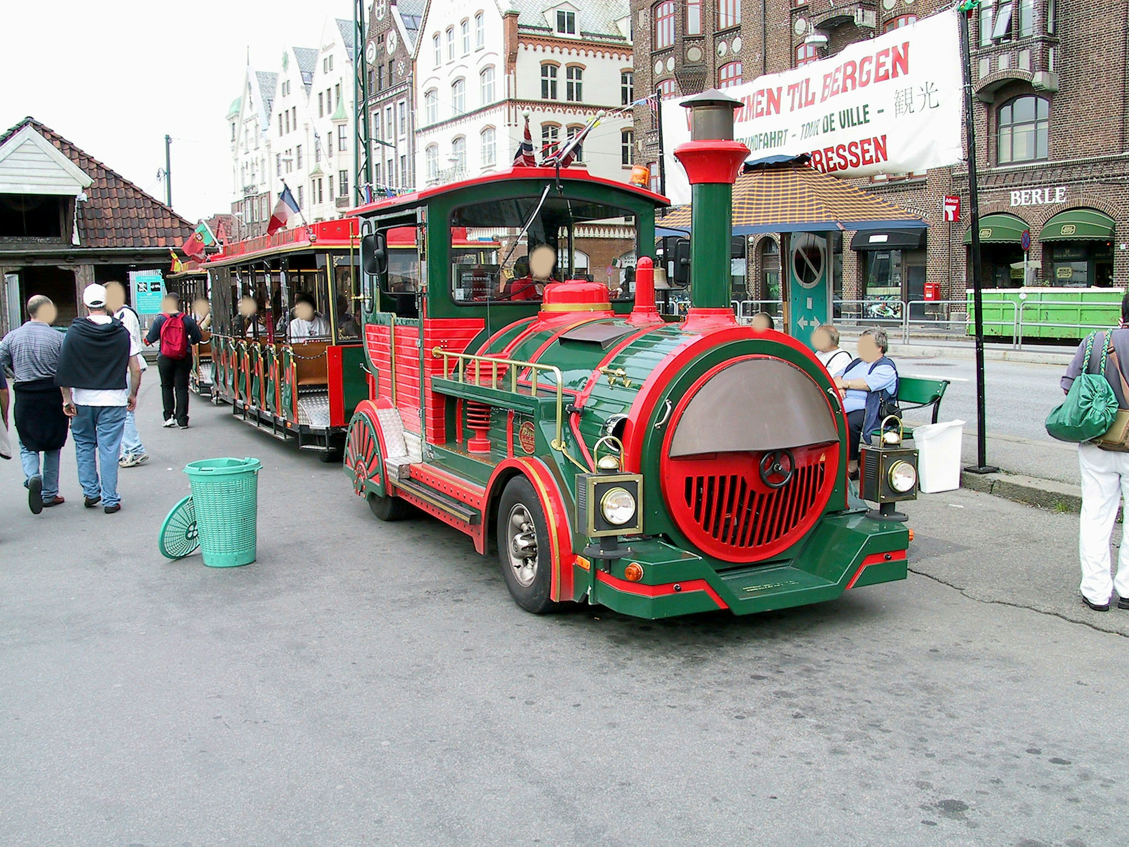 Un train miniature touristique décoré en rouge et vert garé près des gens