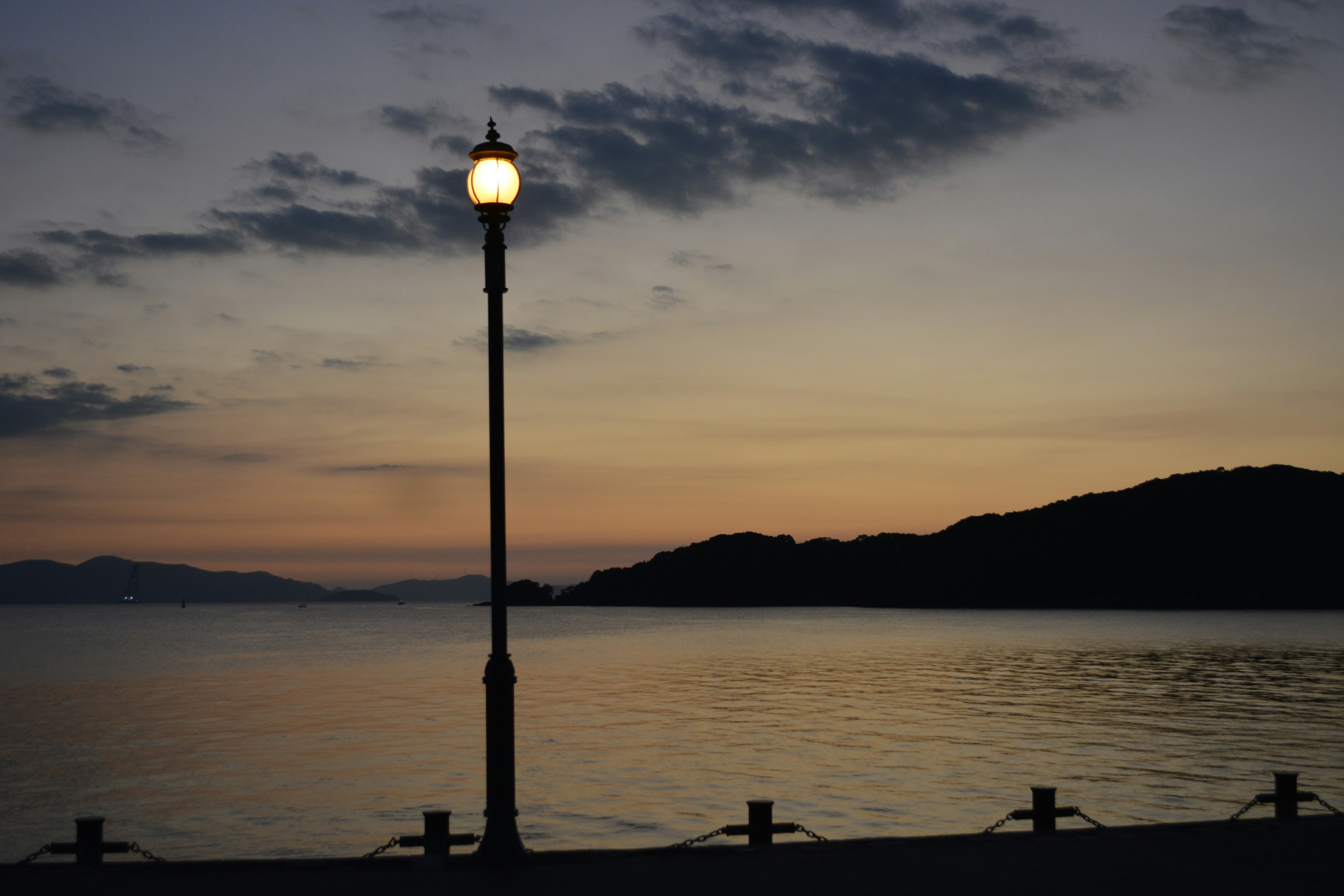 夕暮れ時の海岸線に立つ街灯と静かな水面