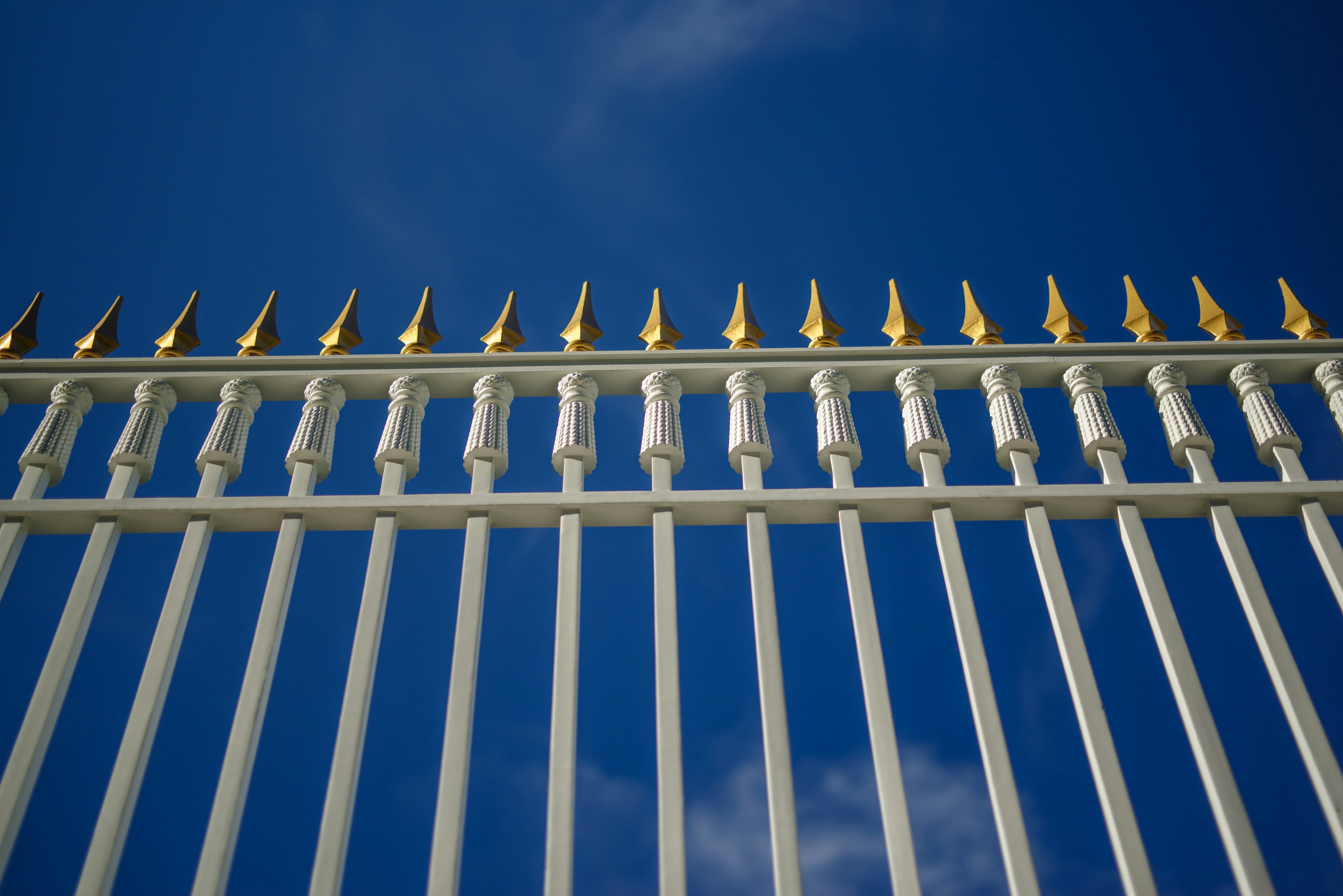 White fence with golden pointed tips against a blue sky