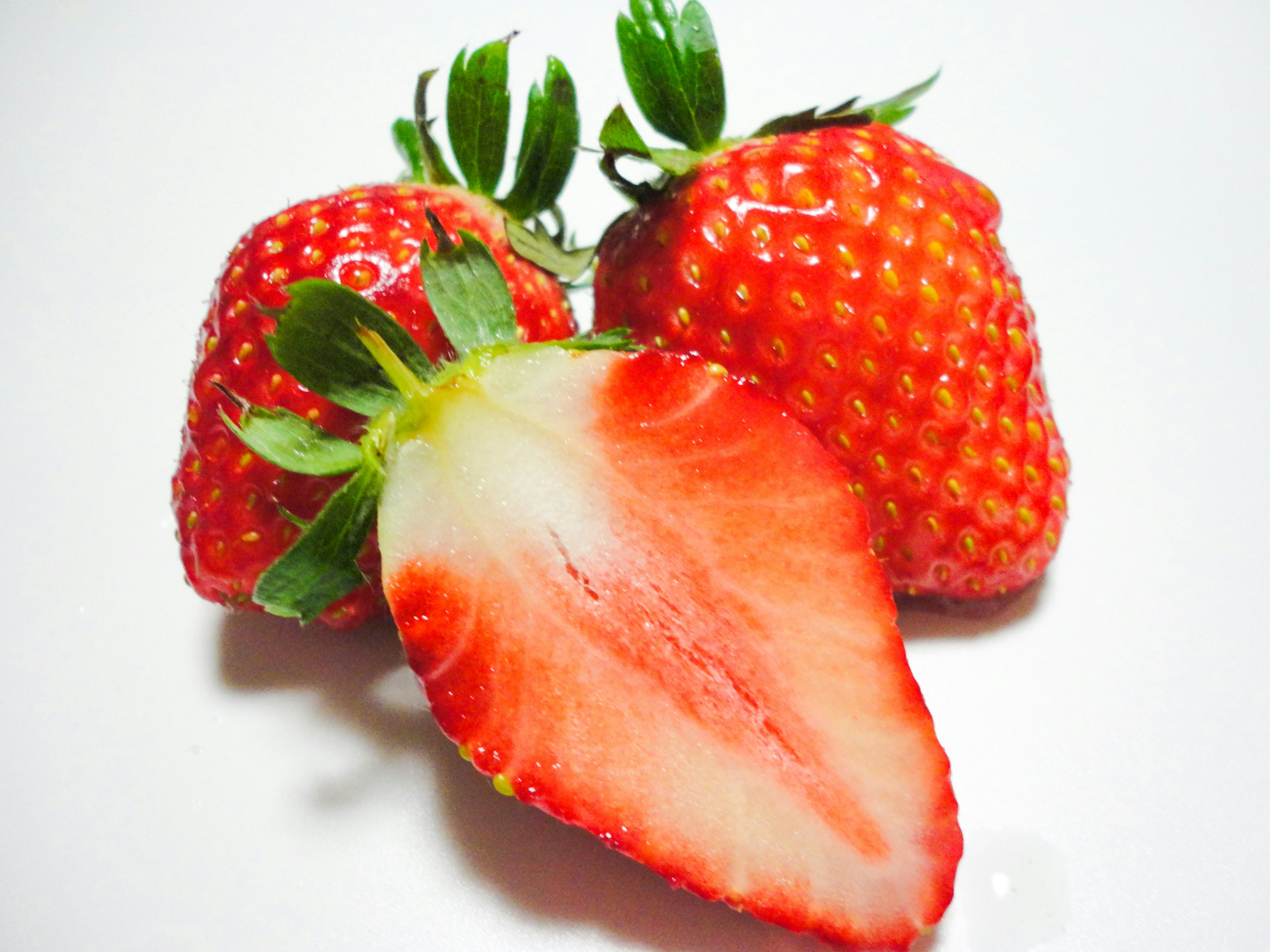 Three vibrant red strawberries with one sliced in half