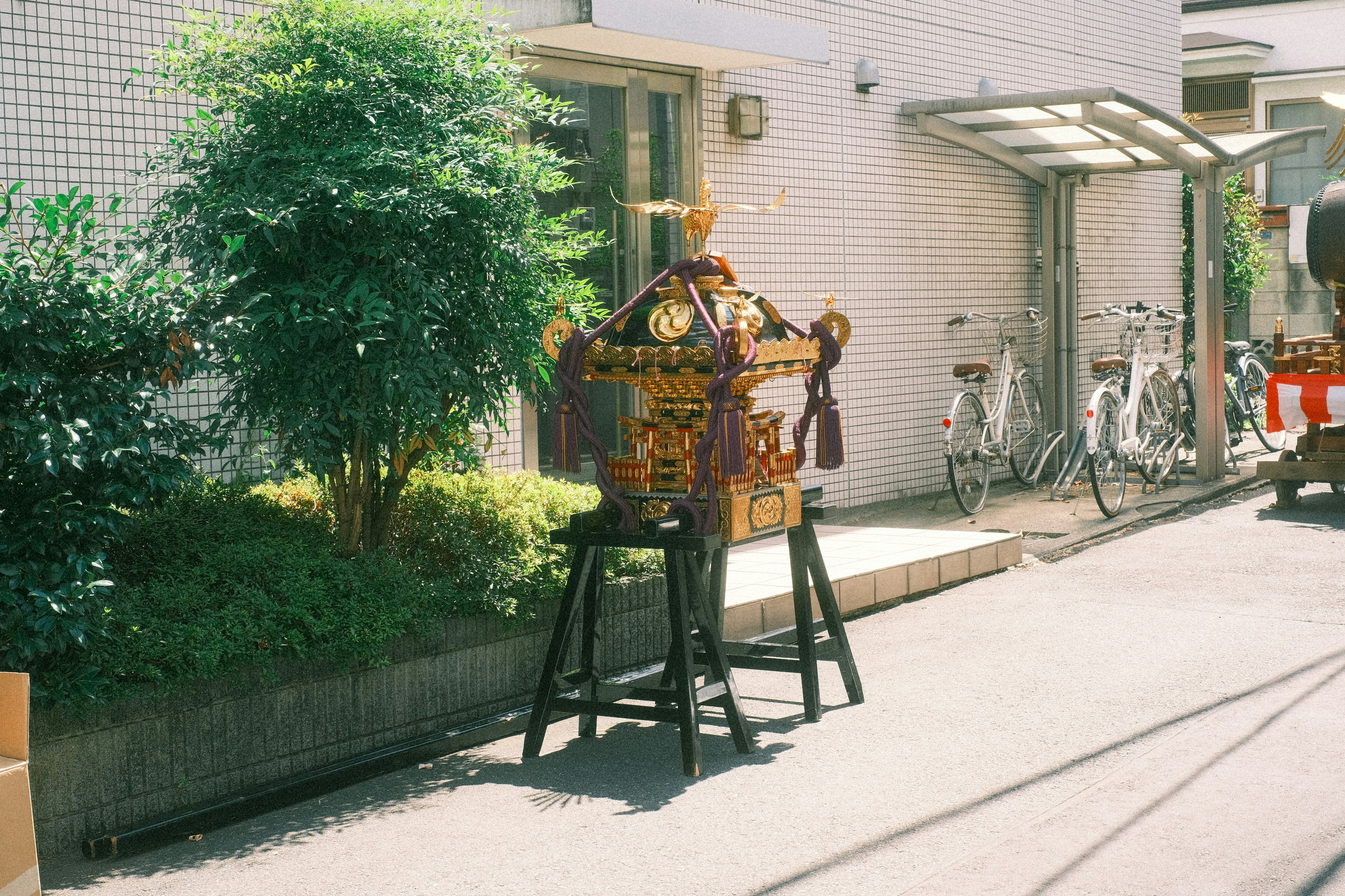 Un mikoshi traditionnel placé dans une rue avec de la verdure et des vélos à proximité