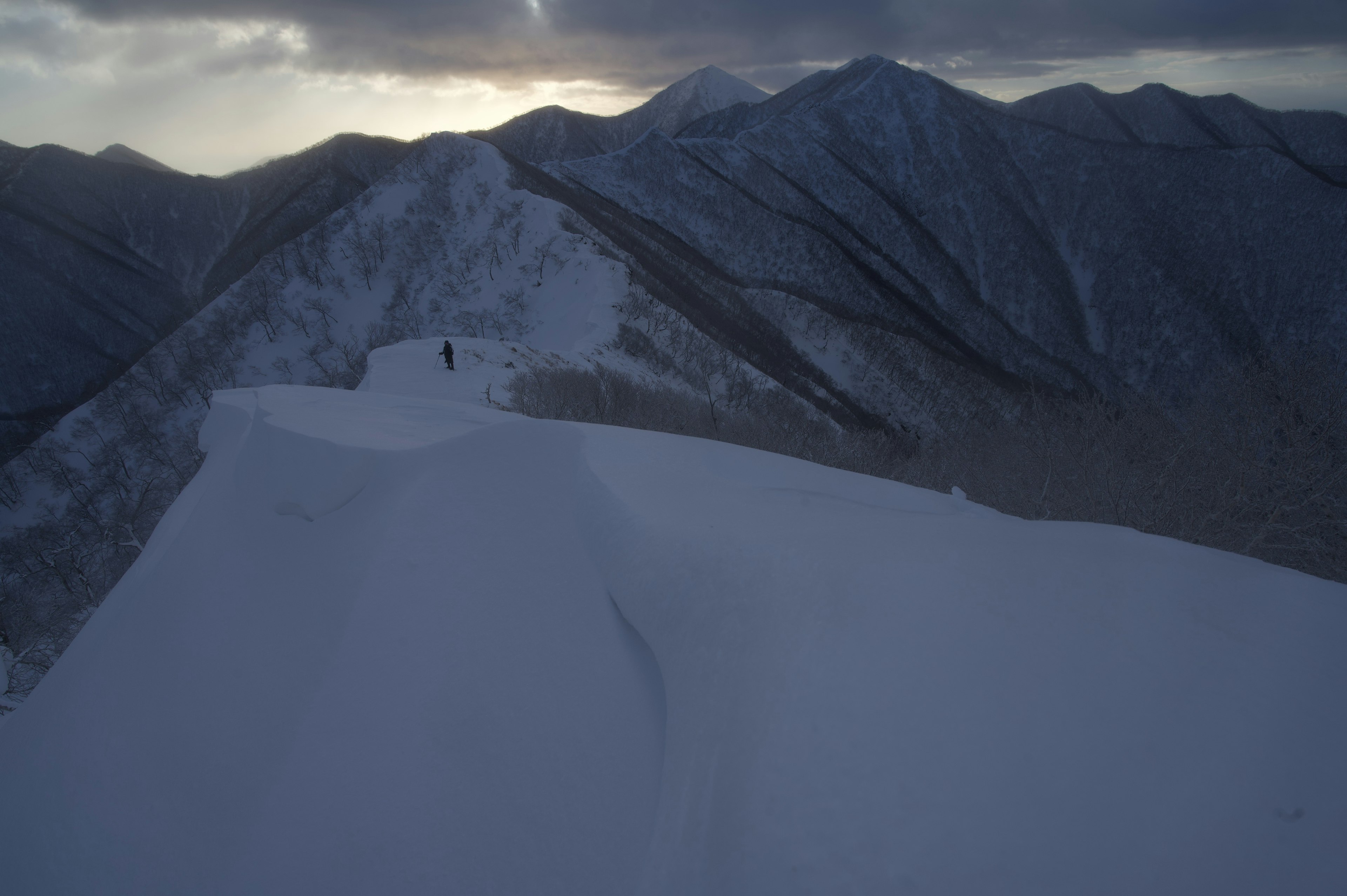 Catena montuosa coperta di neve con la silhouette di un escursionista in lontananza