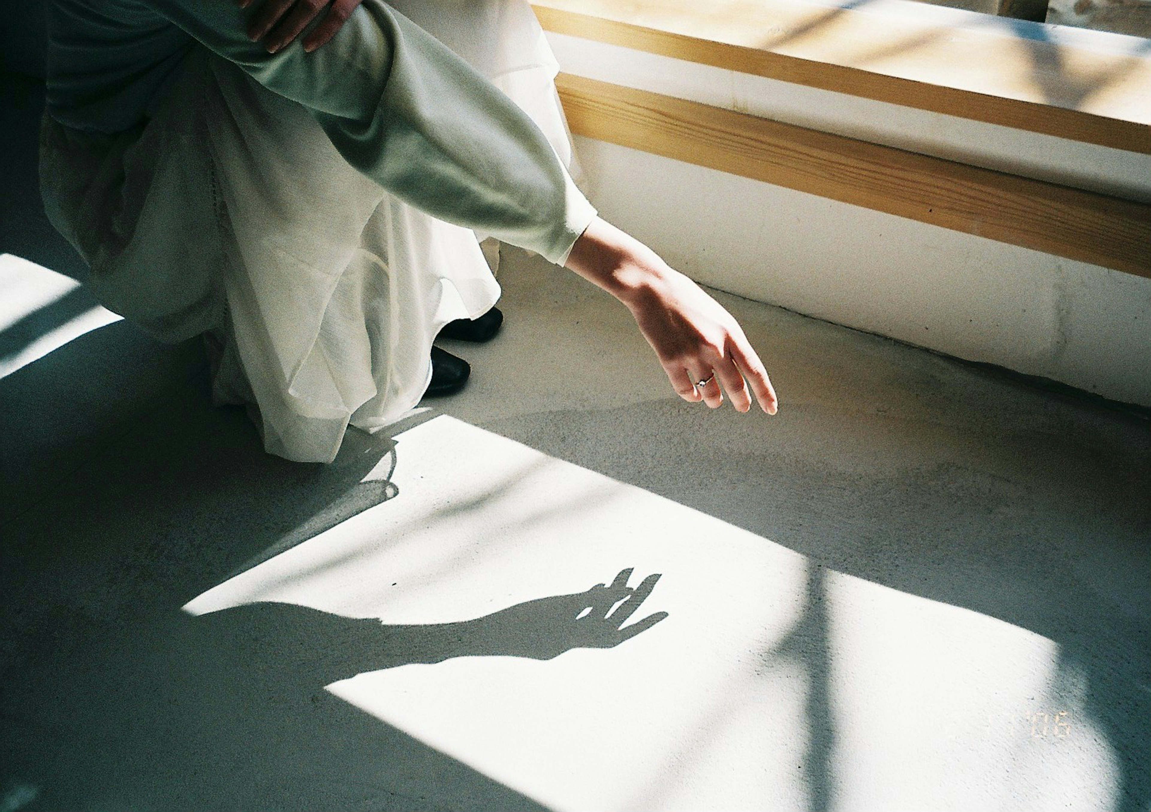 A hand in white clothing reaches toward the floor casting a shadow