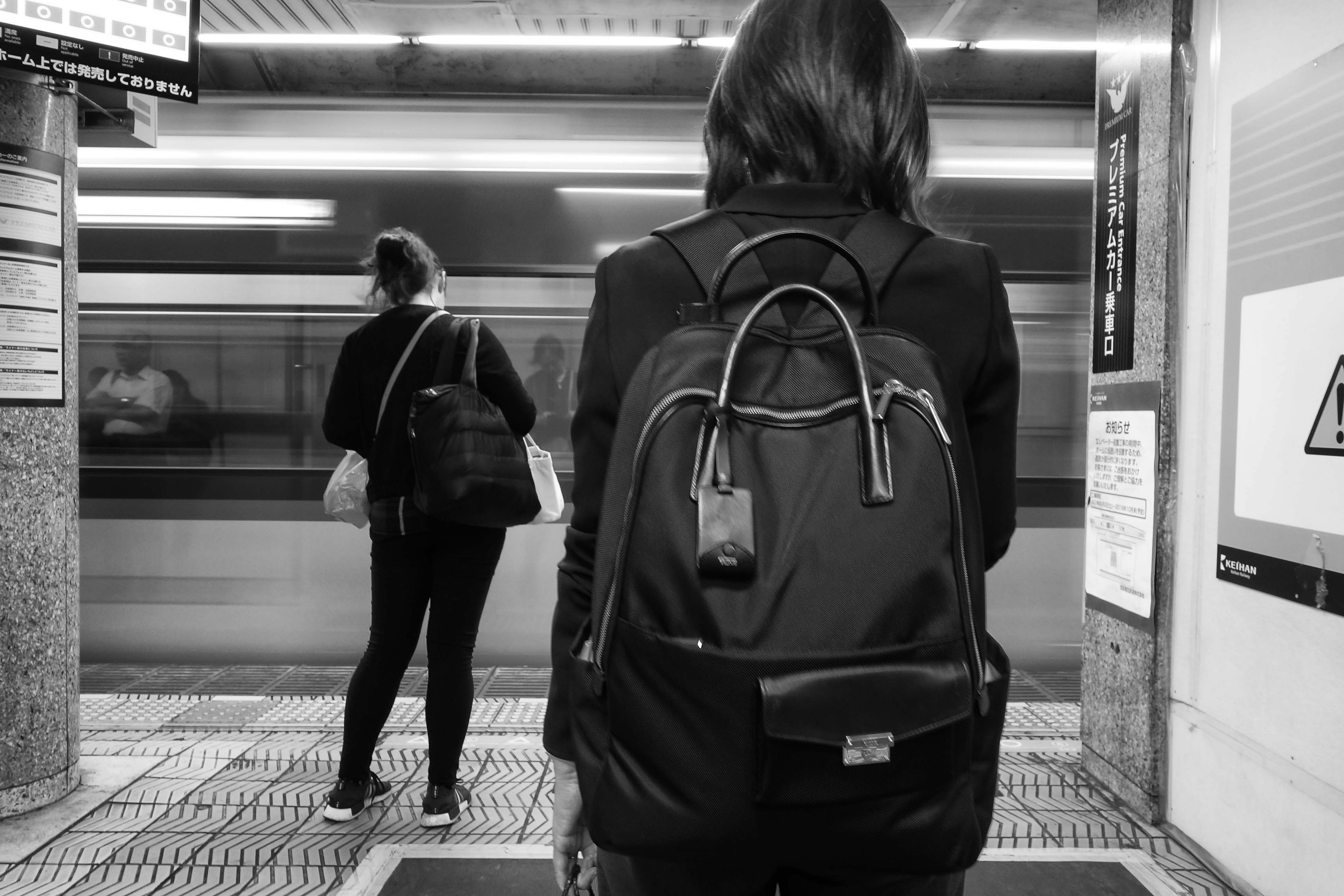 Women waiting on a subway platform with a focus on a backpack