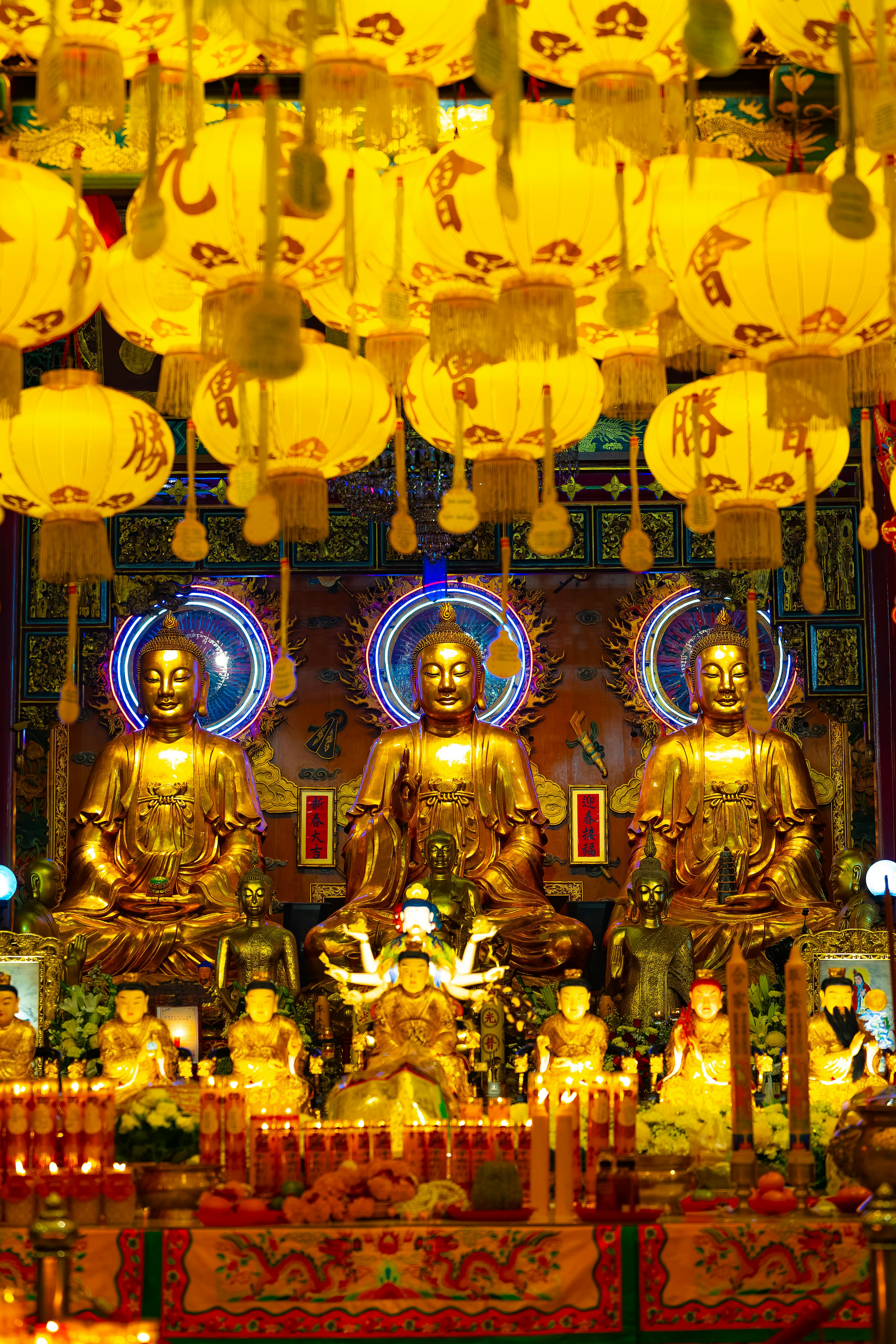 Interior of a temple featuring golden Buddha statues and yellow lanterns