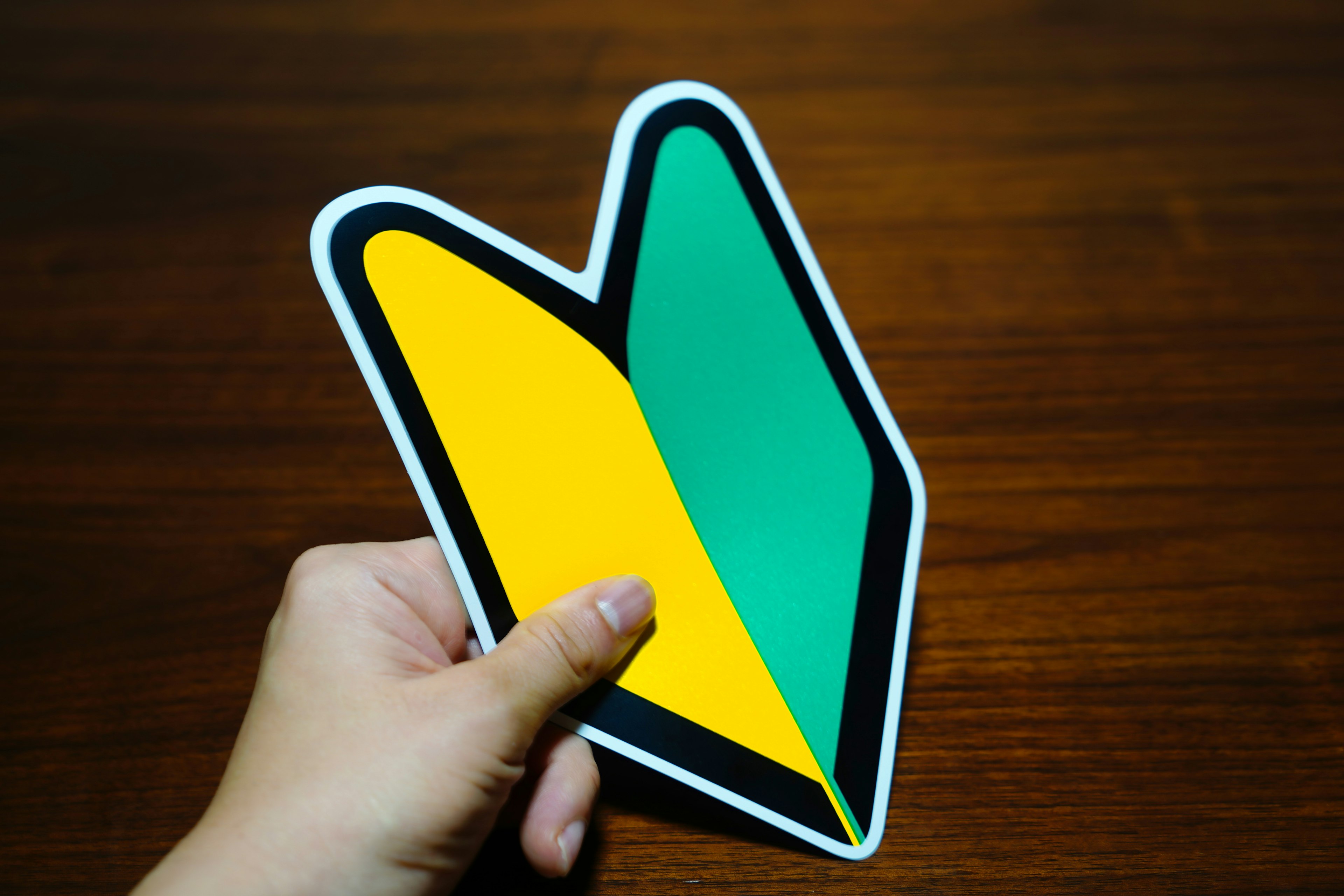 A hand holding a sticker featuring a yellow and green symbol