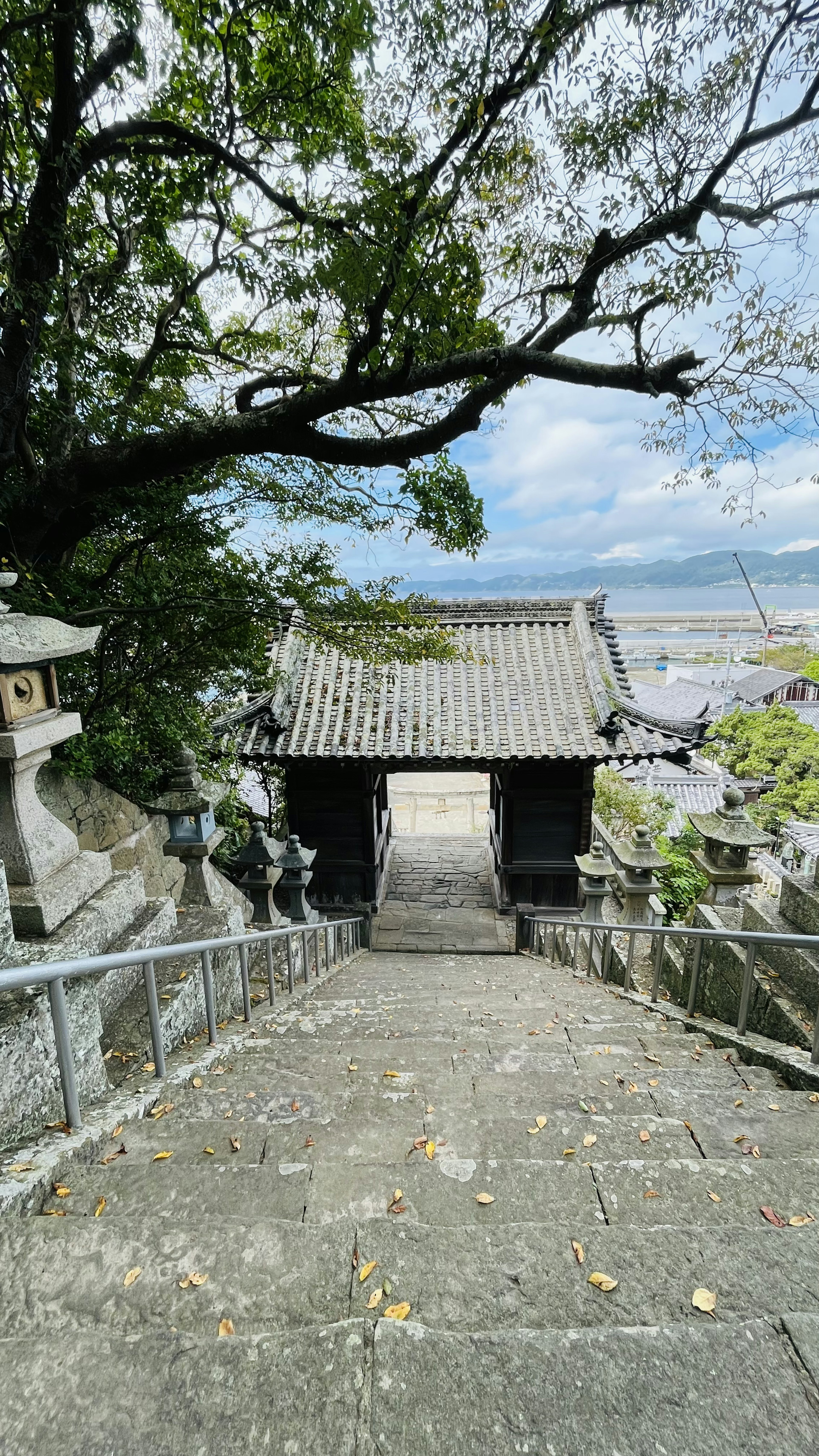 石の階段を下りると見える伝統的な日本の寺院の門と青空