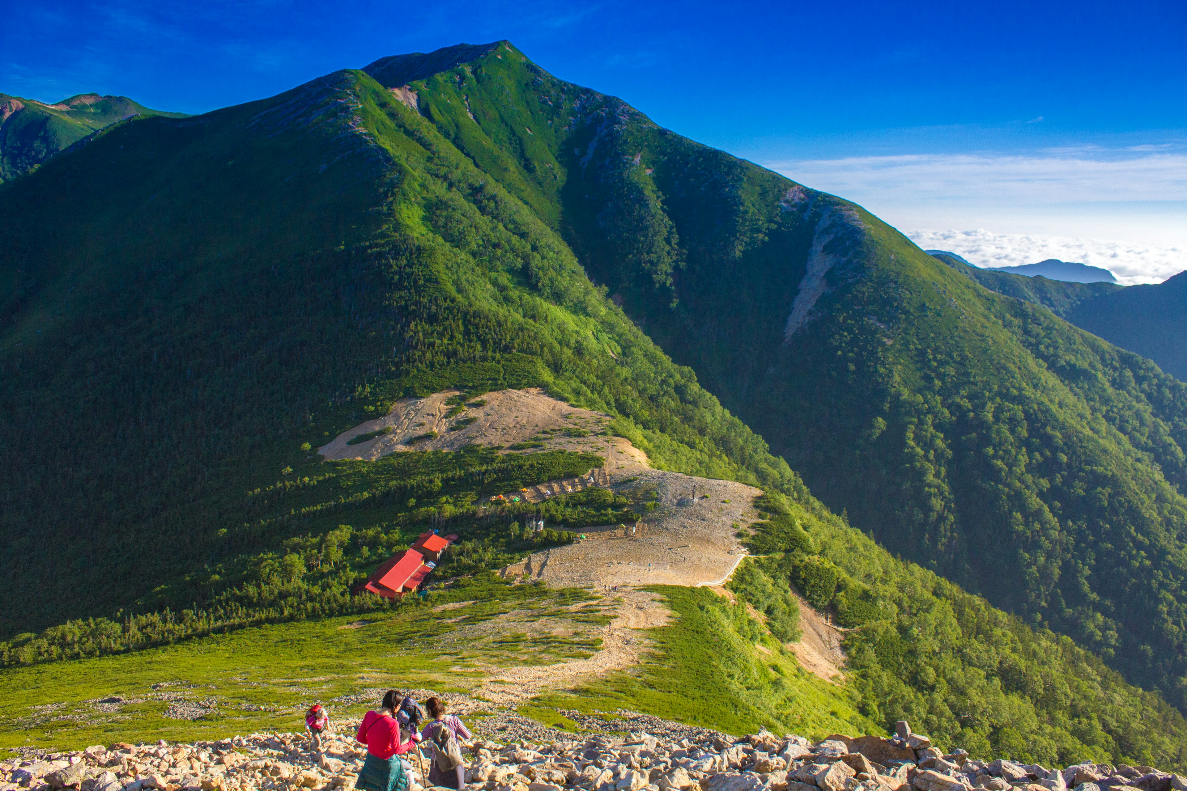 Hikers visible on green mountains under a blue sky