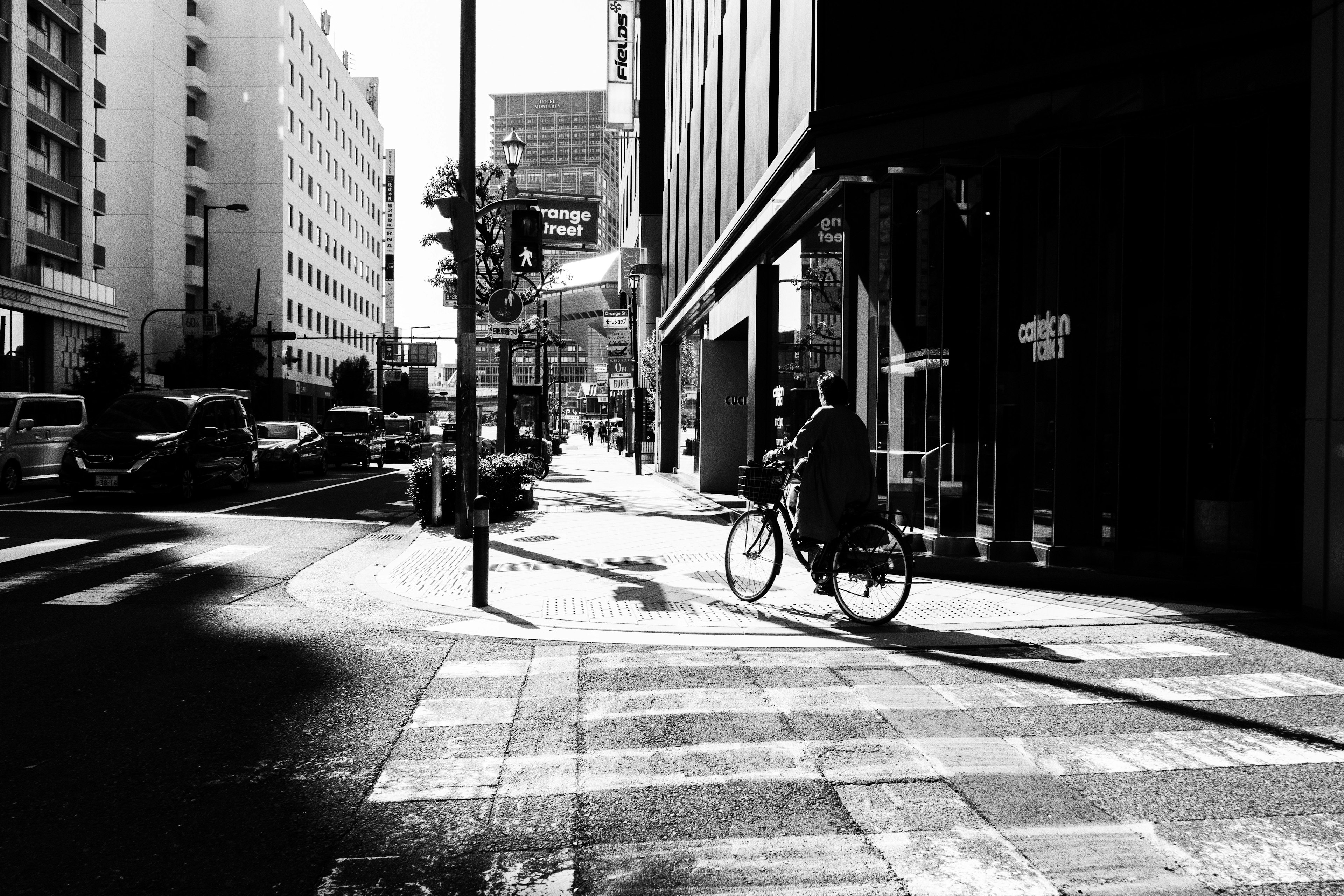 Black and white urban scene with a person riding a bicycle on the sidewalk