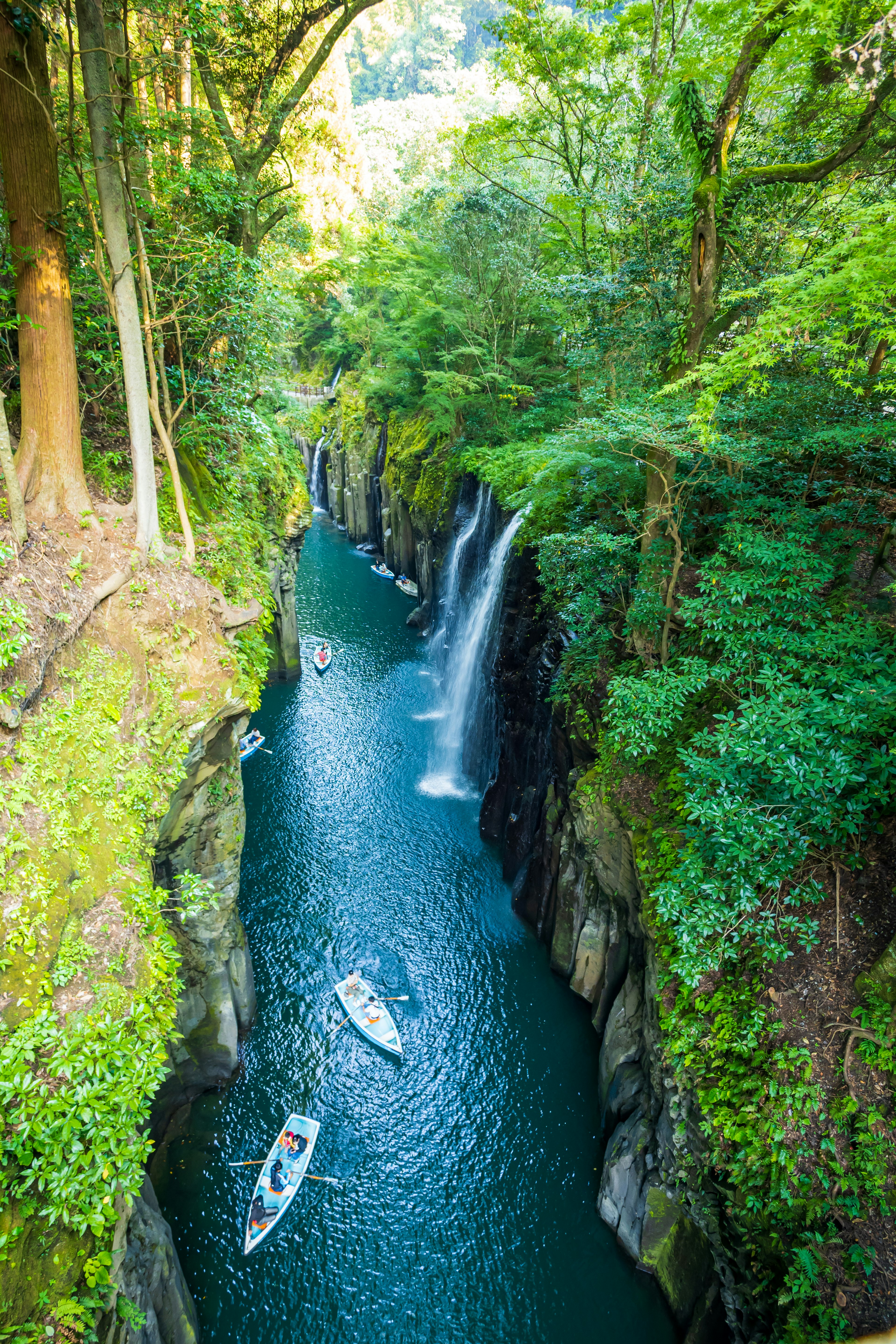 Lush green canyon with flowing river and waterfalls small boats floating in beautiful natural scenery