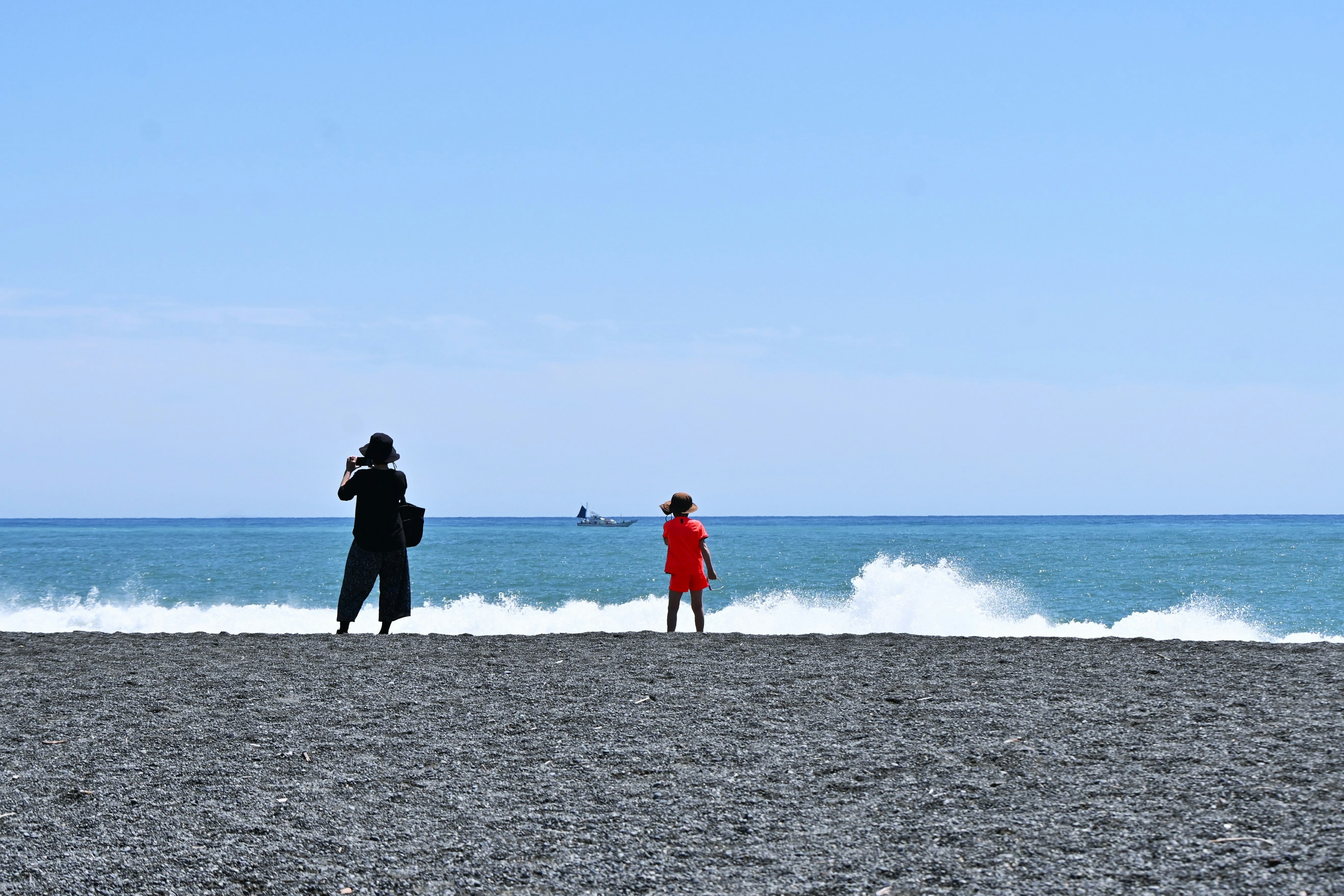 Silhouette of a person in black and a child in red at the beach