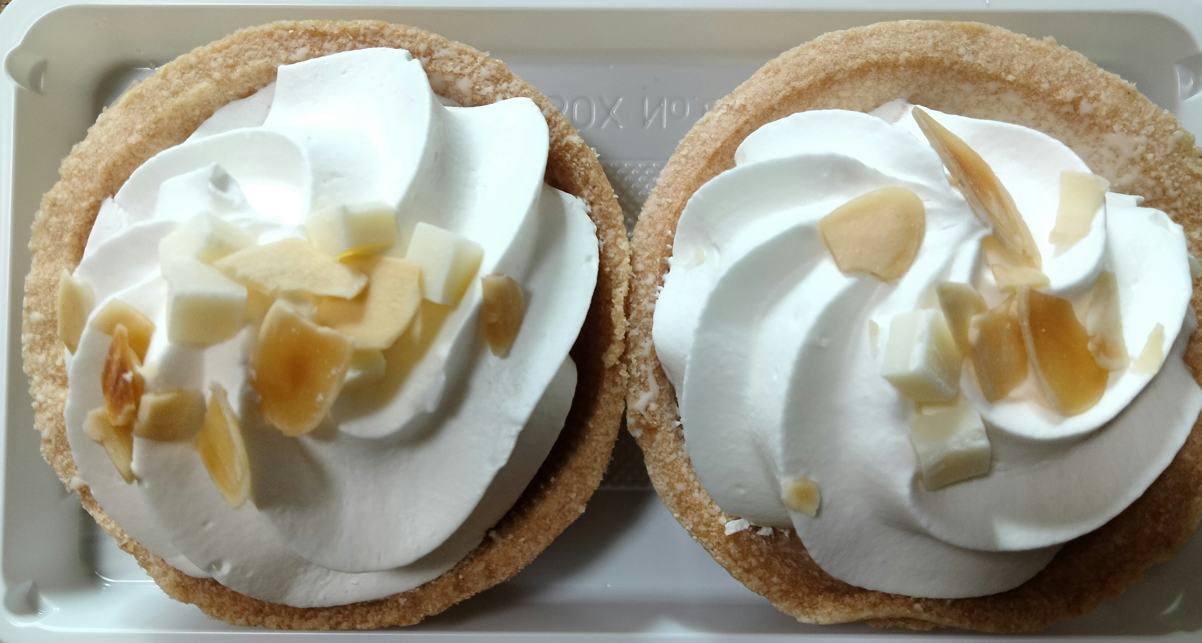 Two cupcakes topped with whipped cream and sliced almonds