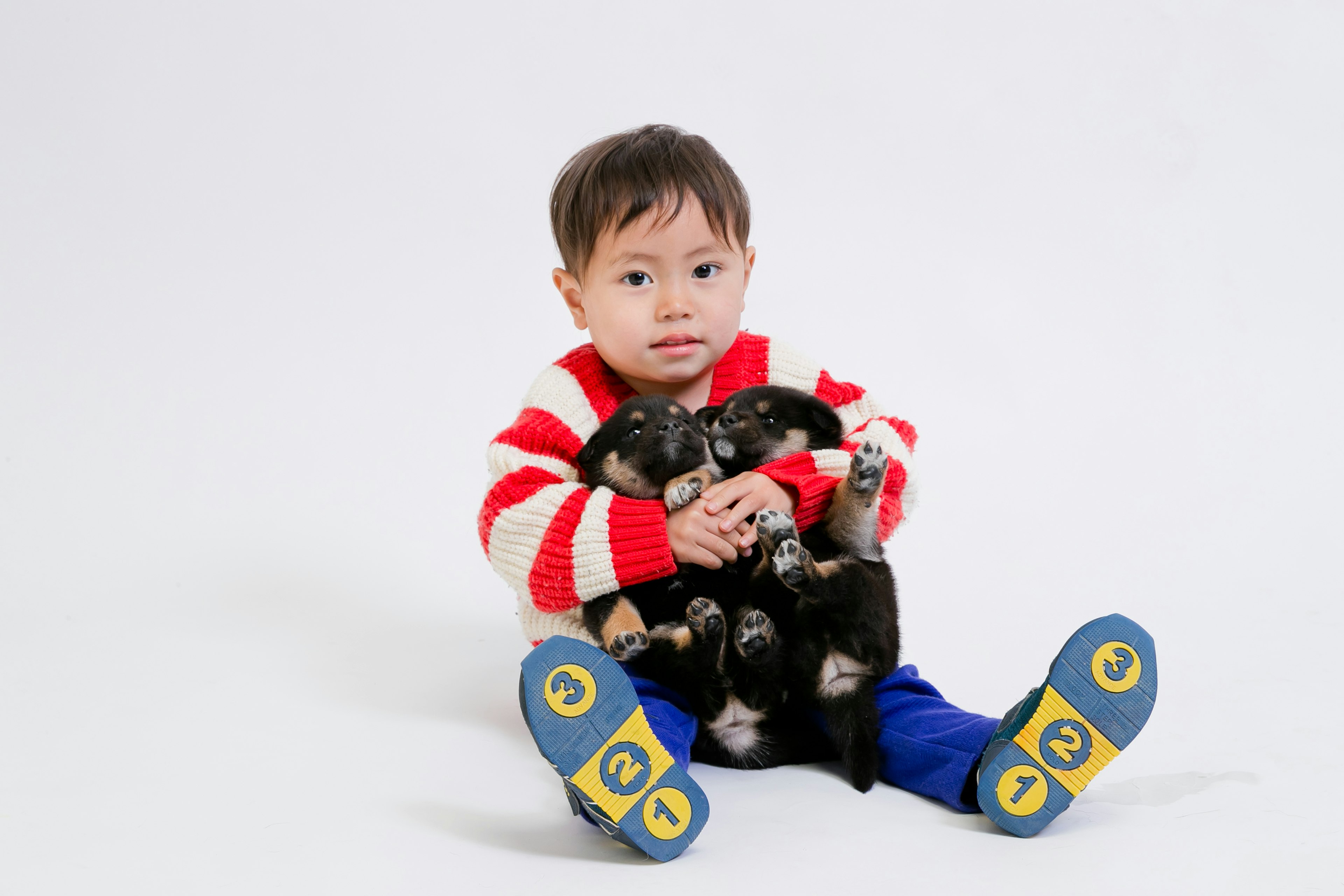 Un bambino con un maglione a righe rosse e bianche che tiene dei cuccioli neri