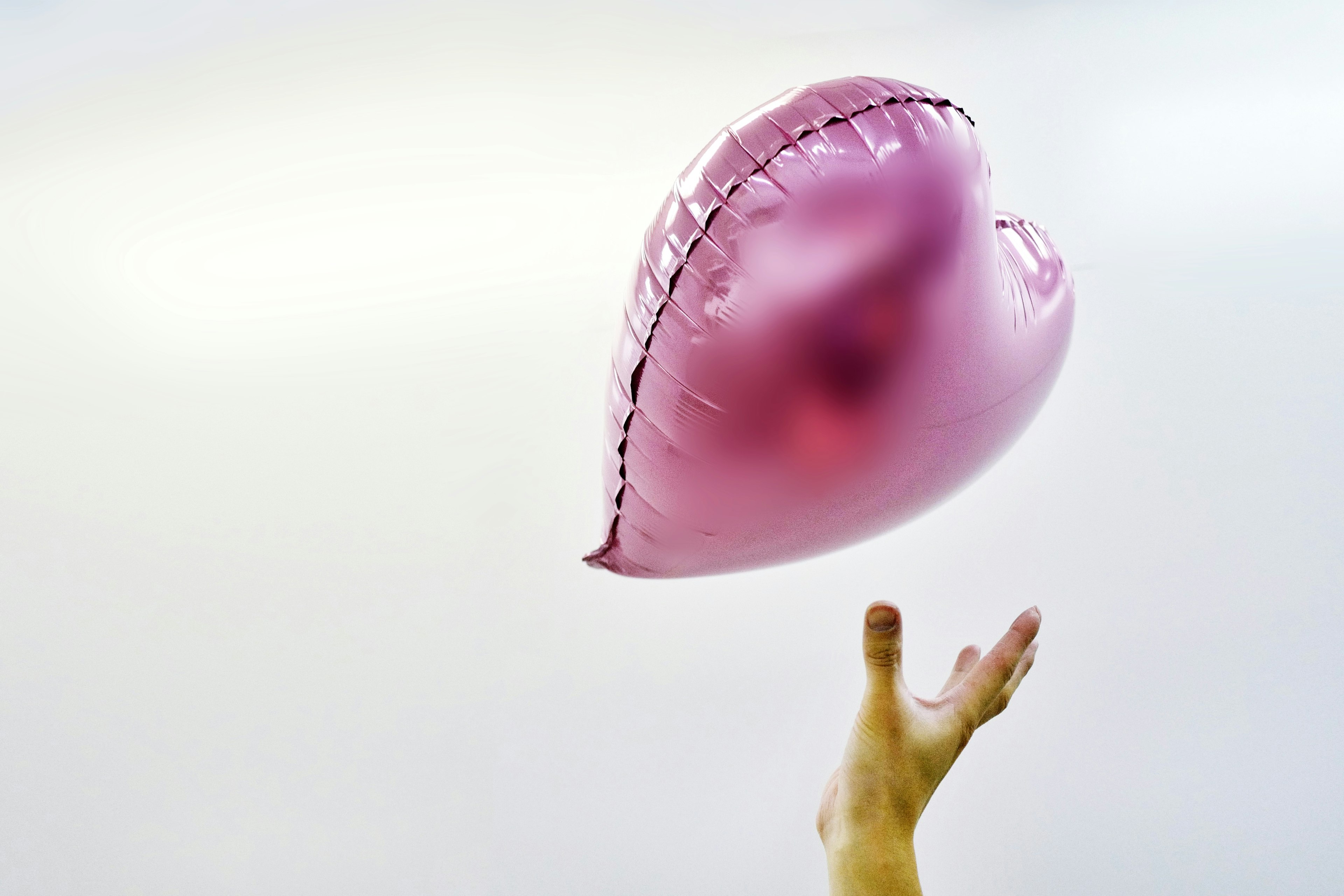 Una mano che si alza verso un palloncino a forma di cuore rosa su sfondo chiaro