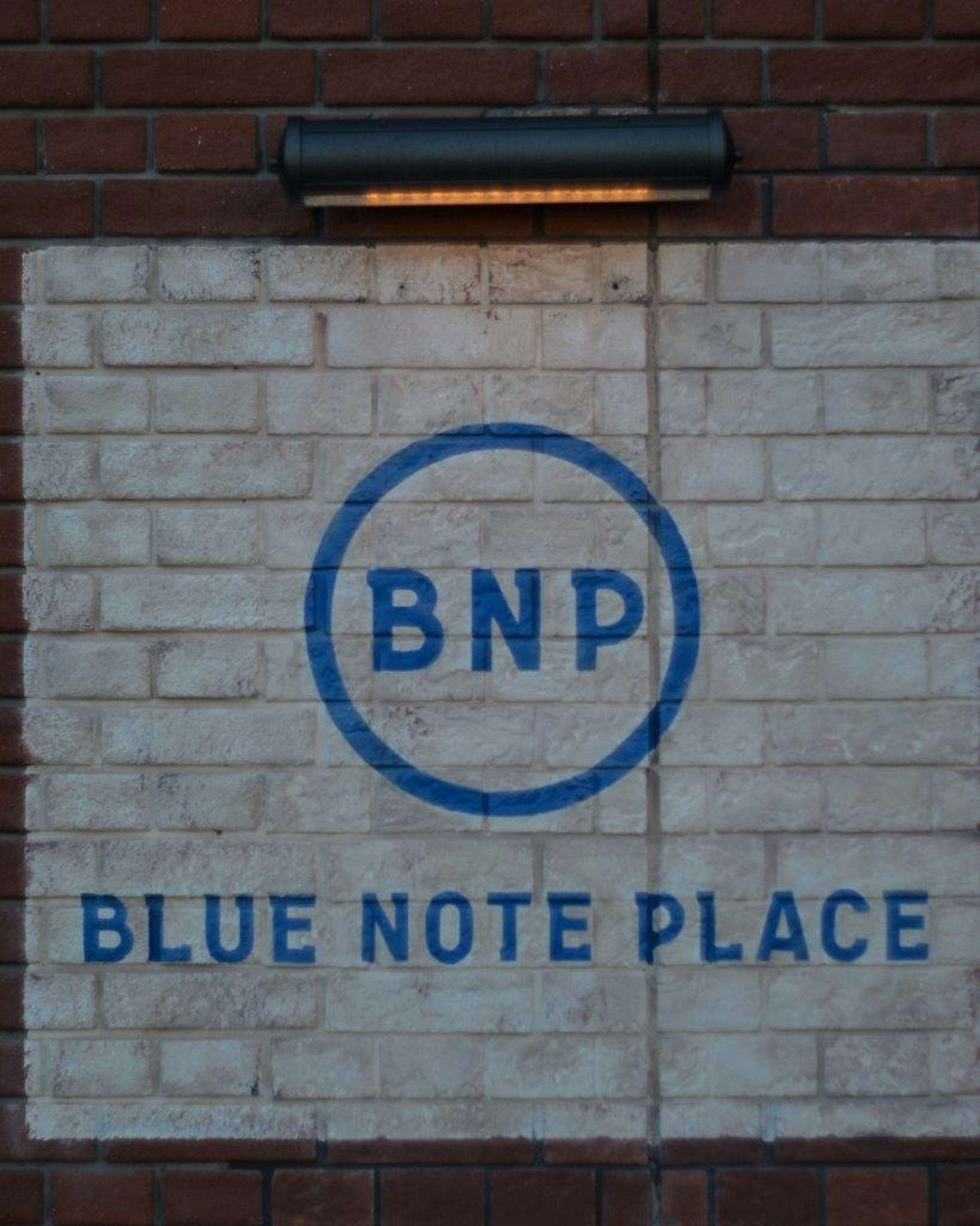 ป้ายสำหรับ Blue Note Place ที่มีตัวอักษรสีน้ำเงินบนผนังอิฐ