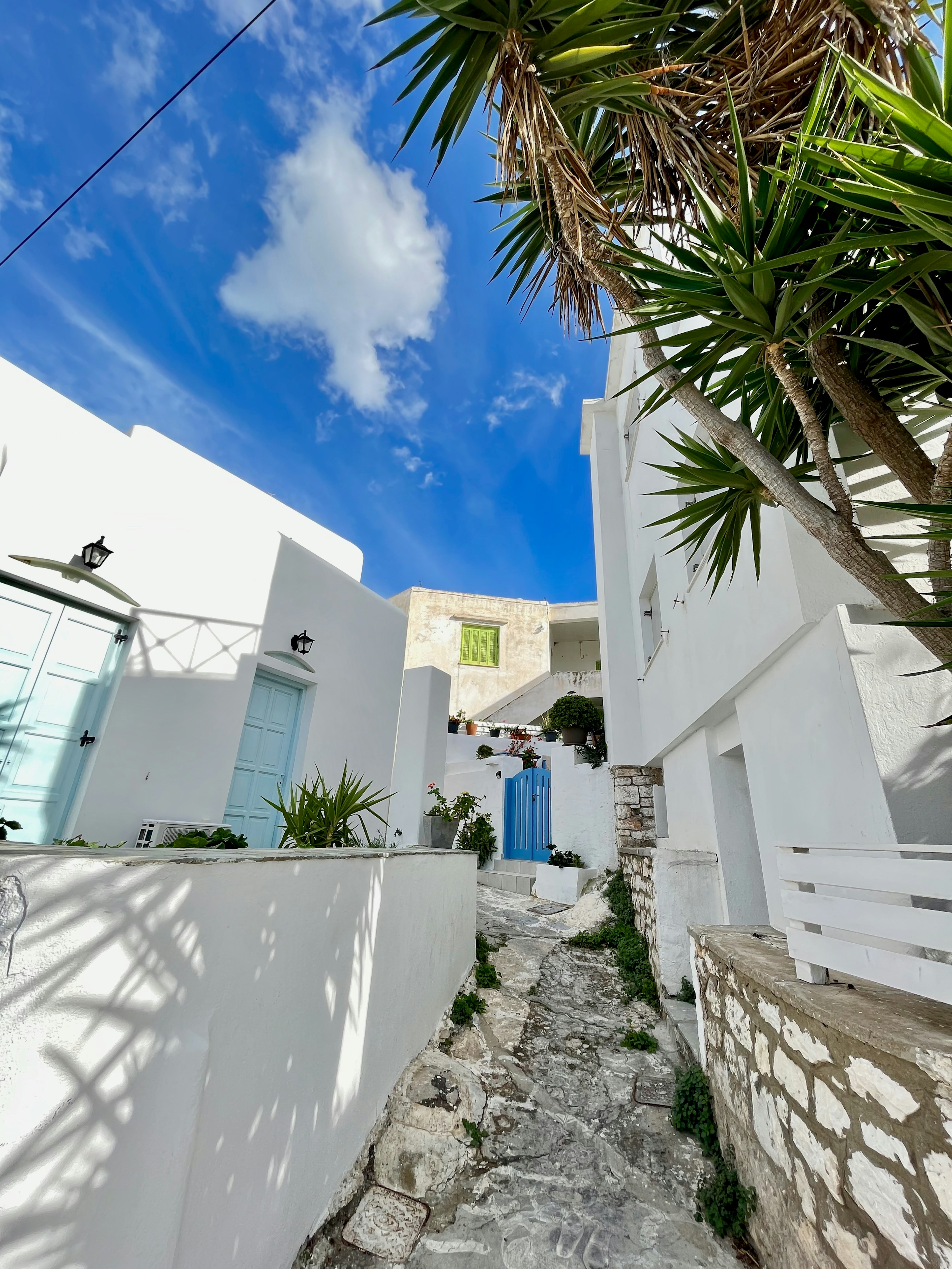 Narrow cobblestone alley with white buildings and blue sky