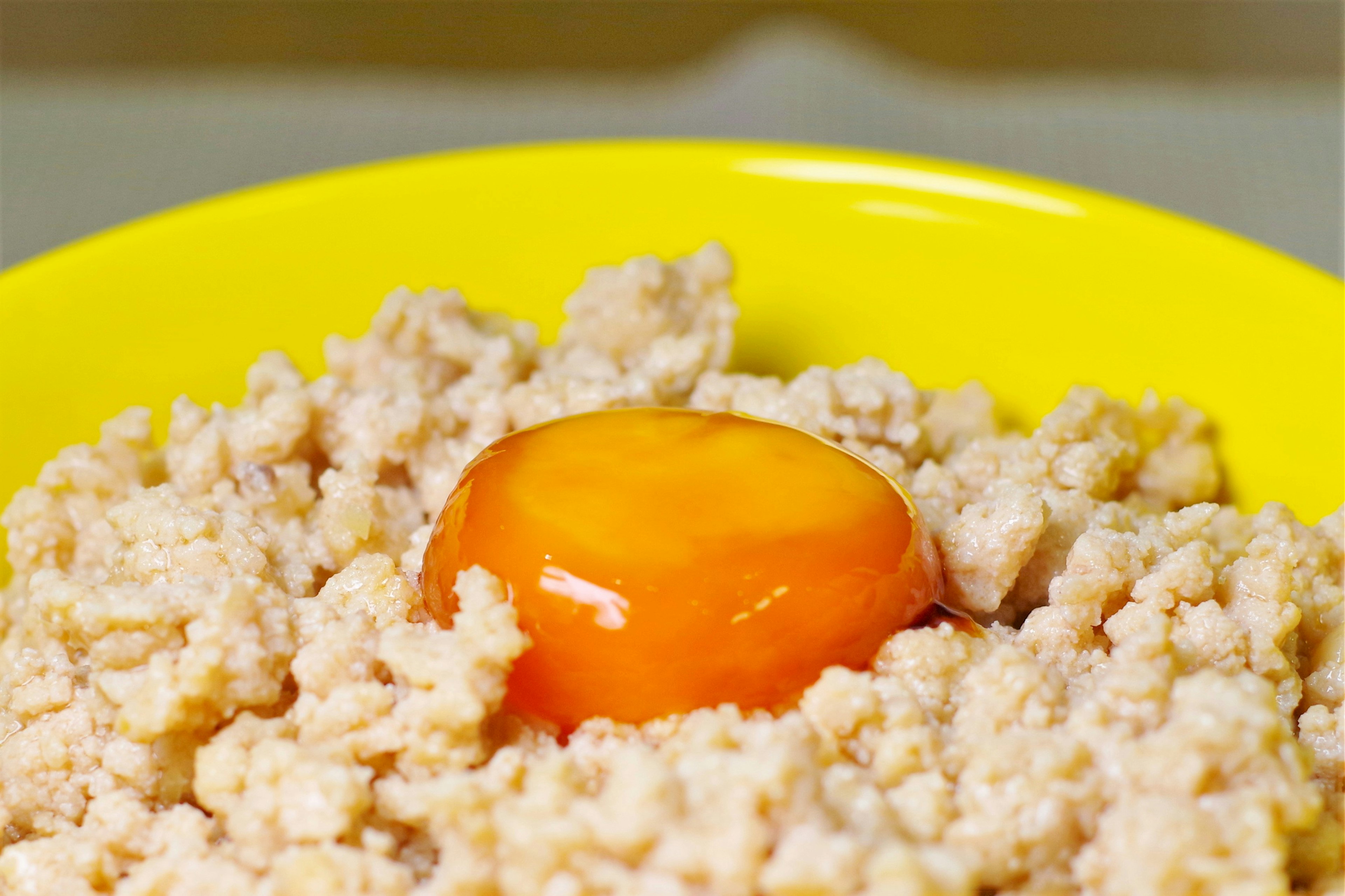 Bol amarillo lleno de alimento similar a granos coronado con una yema de huevo