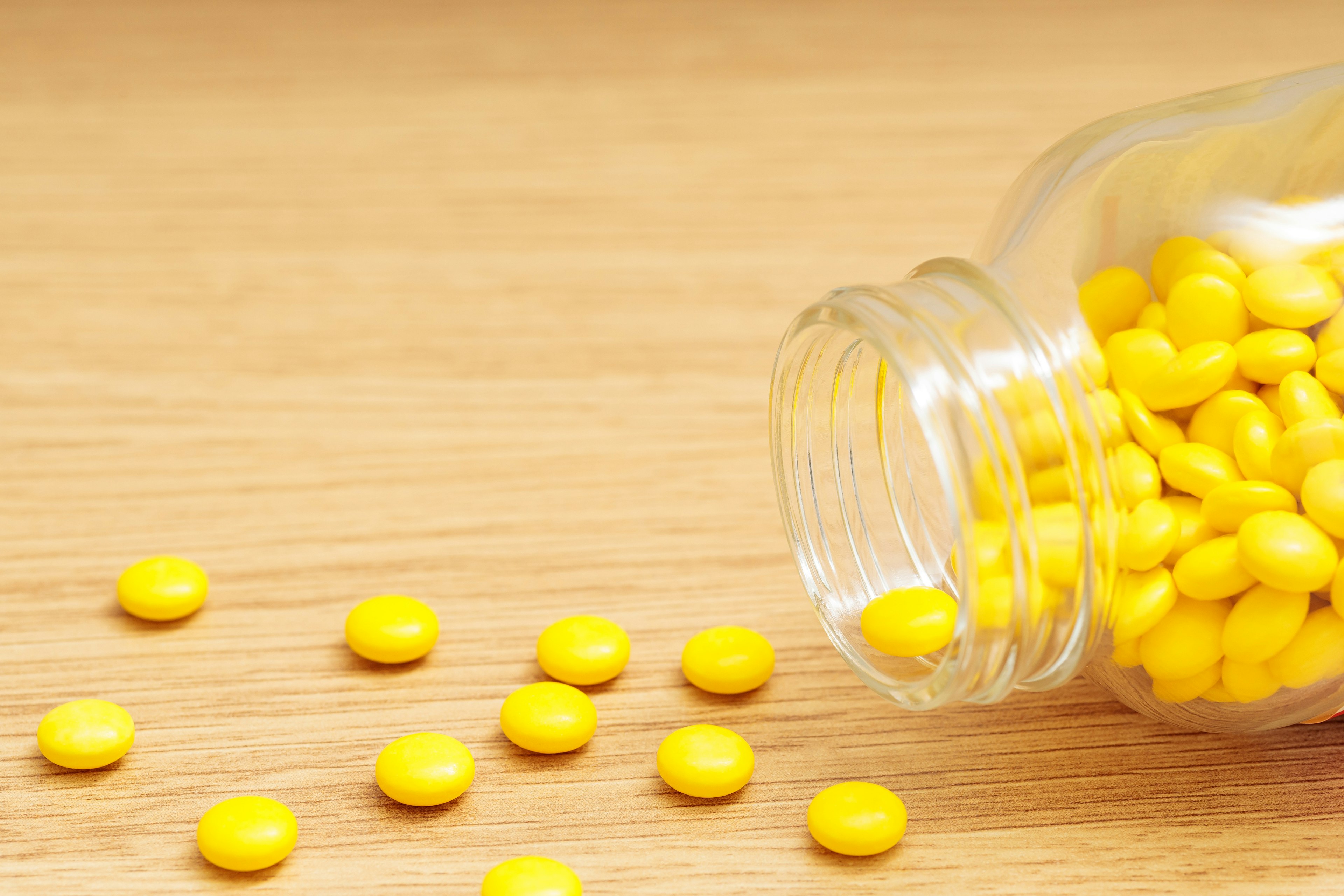 A glass jar spilled with yellow pills on a wooden surface