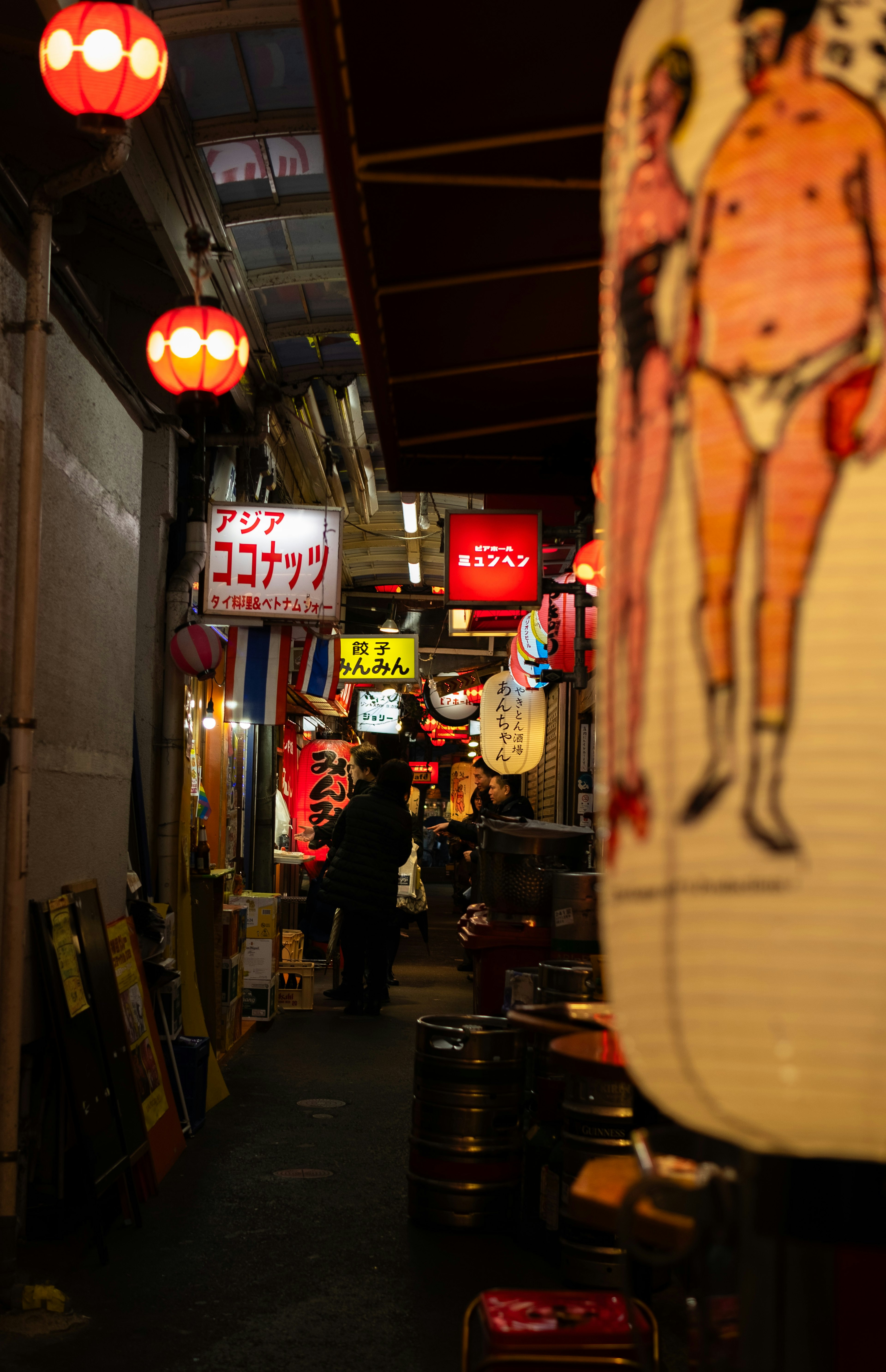 A narrow alleyway featuring lanterns and various shop signs