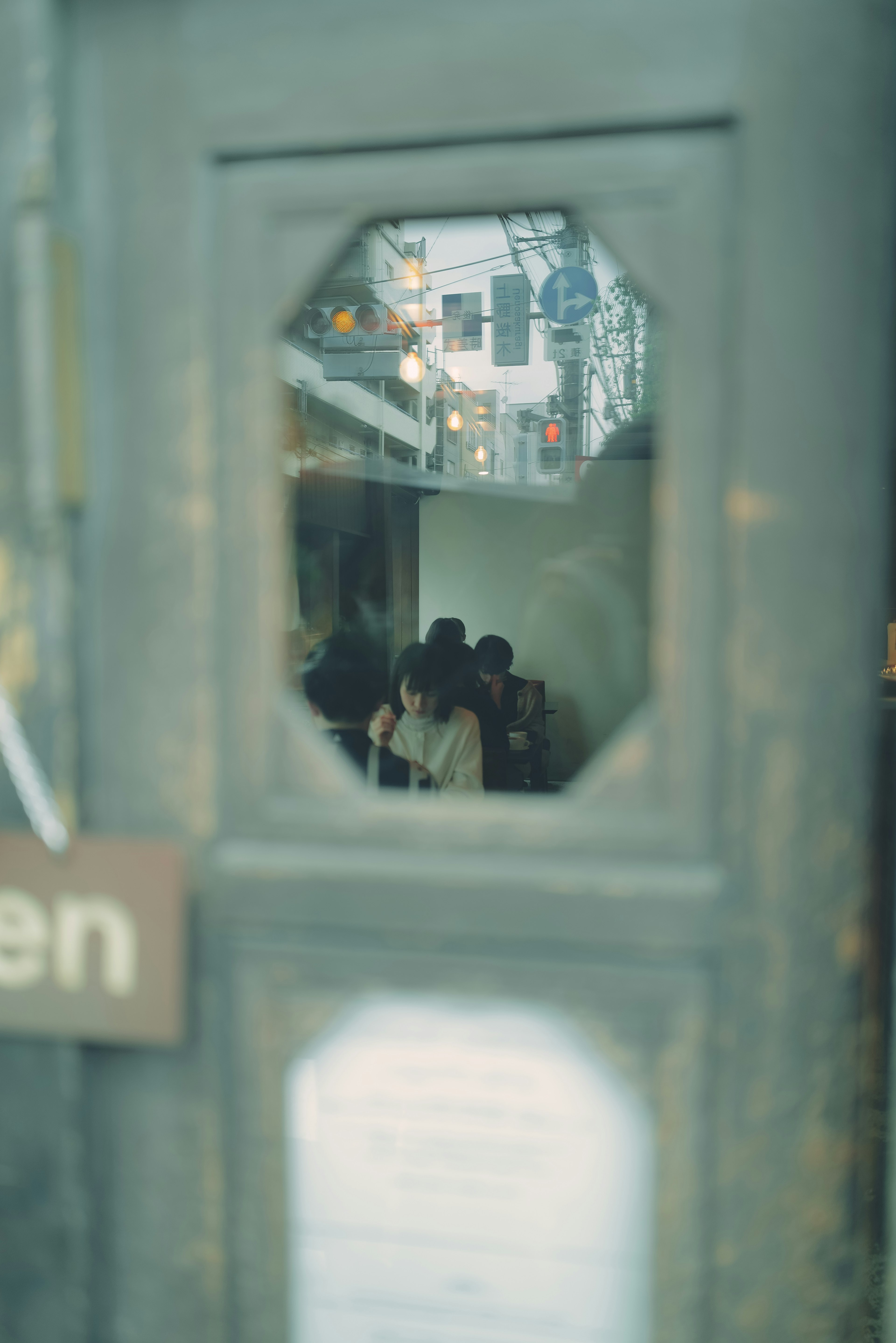 View through an octagonal window of a door showing people and interior of a cafe