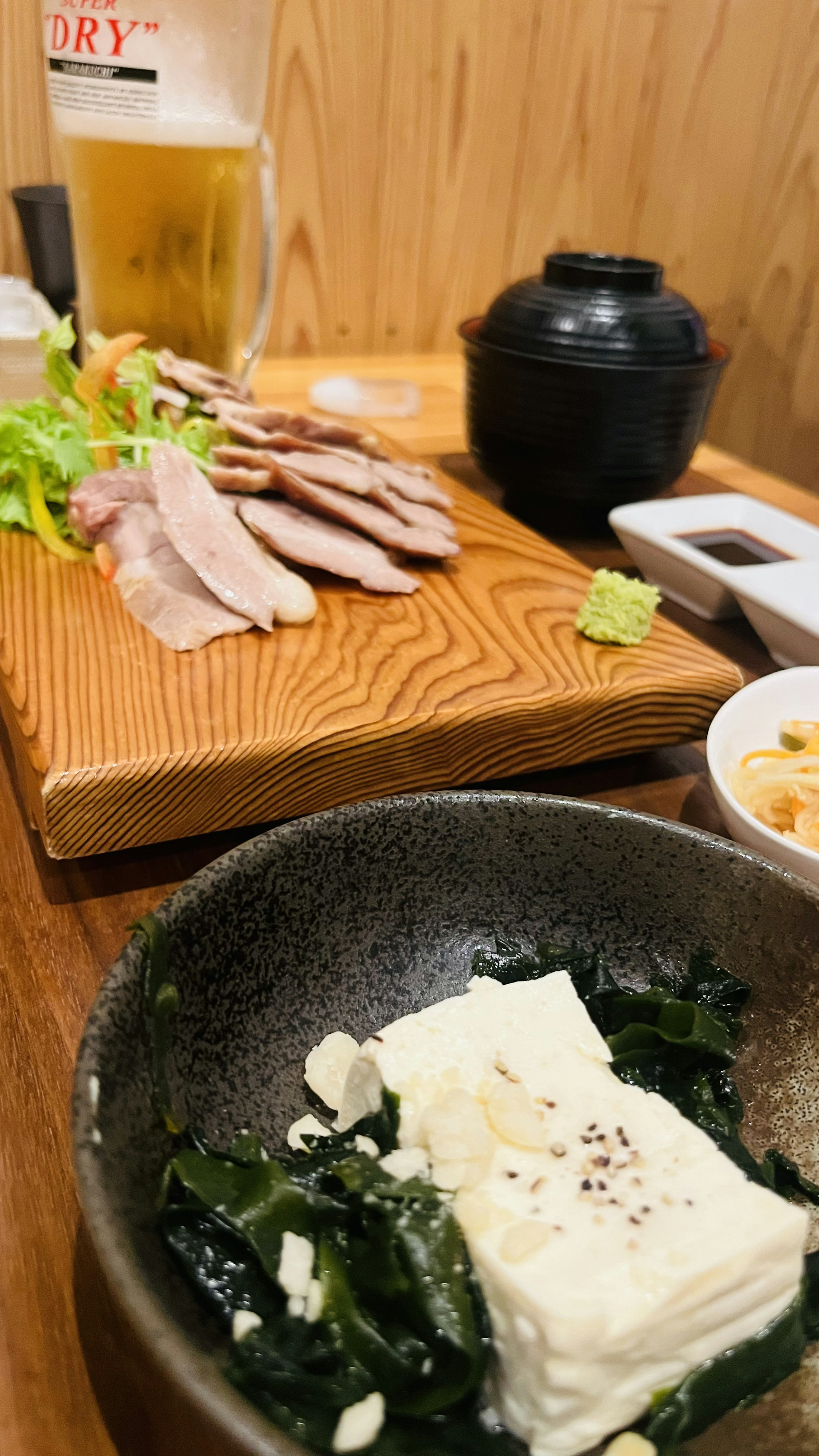 Japanese meal set on a table featuring tofu and seaweed salad with grilled meat and beer